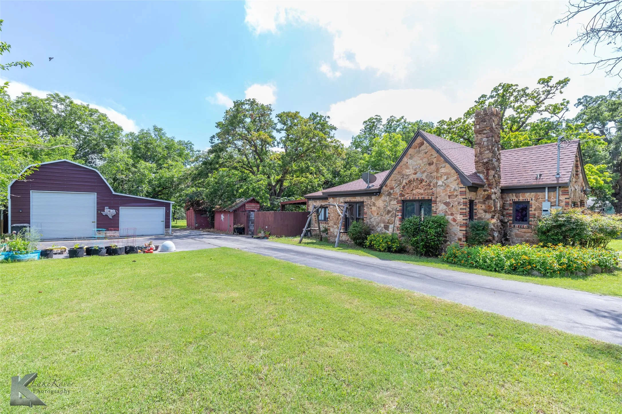 View of front facade with stone siding, a garage, a front yard, an outdoor structure, and driveway