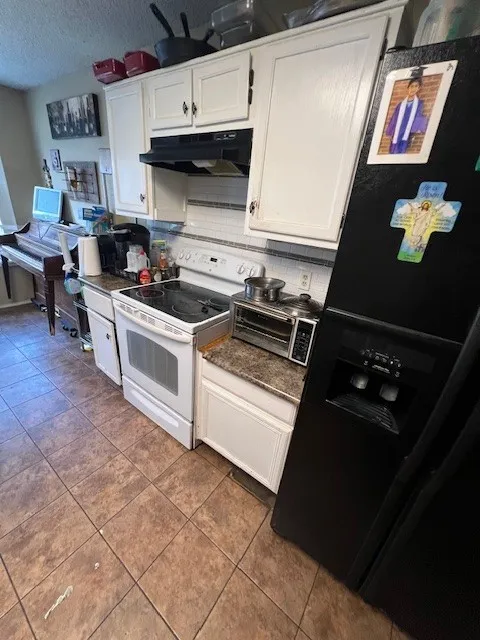 Kitchen featuring under cabinet range hood, white electric range, white cabinetry, dark countertops, and a textured ceiling