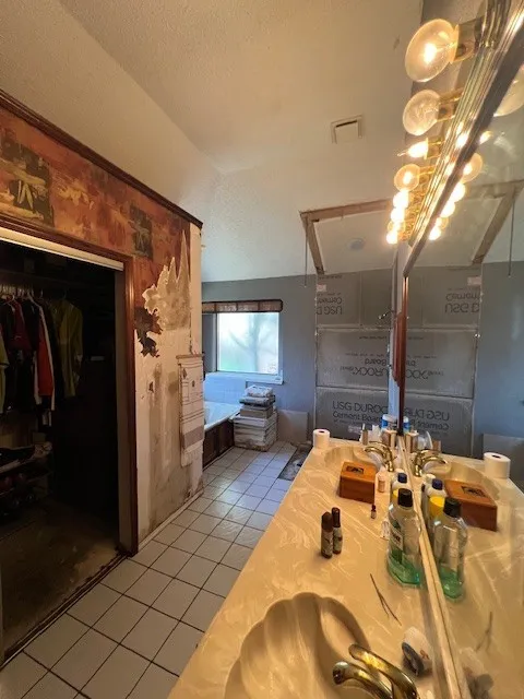 Full bath with tile patterned flooring, double vanity, a textured ceiling, and a walk in closet
