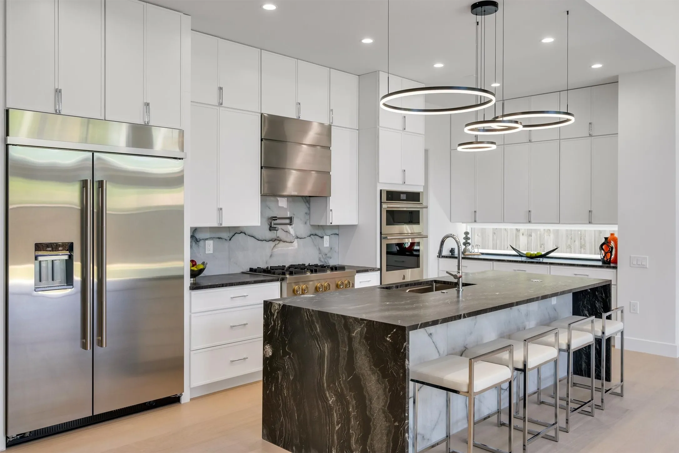Kitchen featuring appliances with stainless steel finishes, wall chimney range hood, a sink, light wood finished floors, and tasteful backsplash