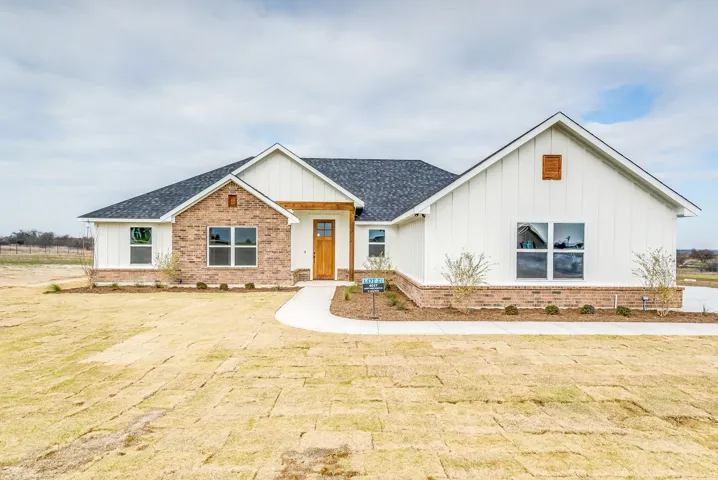 Modern farmhouse style home with board and batten siding, brick siding, roof with shingles, and a front yard