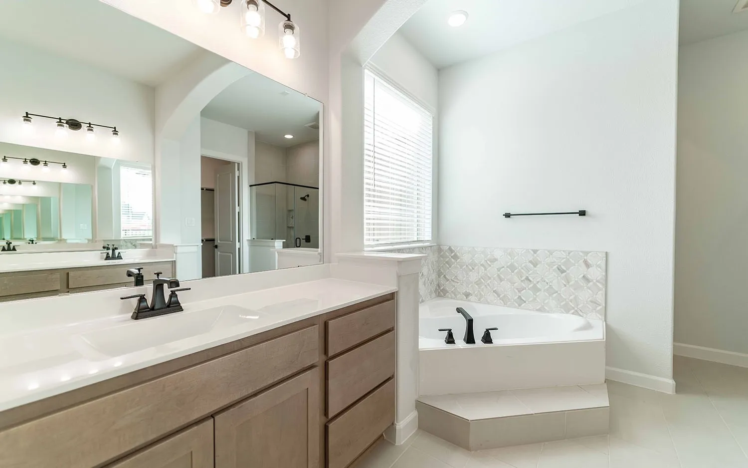 Dual vanity with integrated sinks, light wood-finish cabinetry, and matte black fixtures