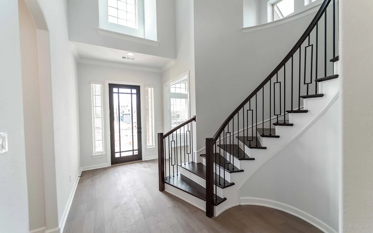 Two-story entry featuring wood-finish flooring, a dark wood-paneled entry door, and a curved staircase with dark wood treads and wrought iron balusters