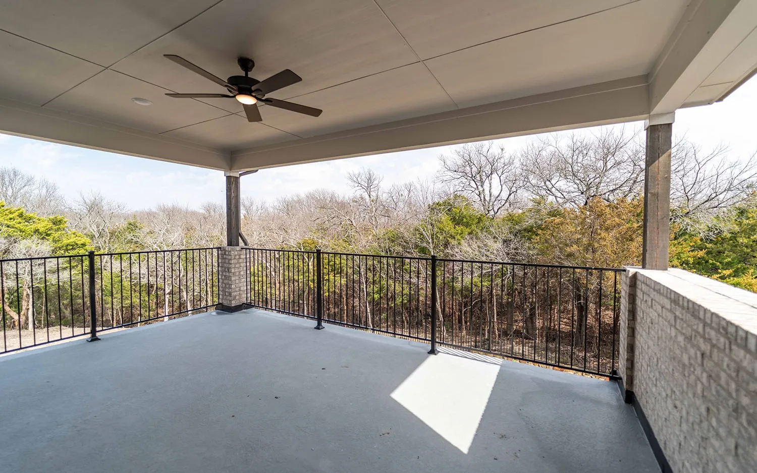 Expansive covered outdoor living space featuring a ceiling fan, recessed lighting, brick pillar accents, and a black metal railing