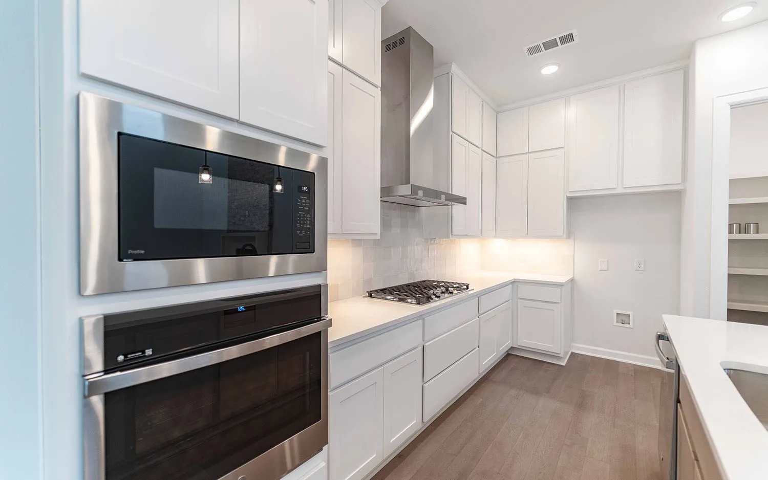 Kitchen featuring white shaker cabinetry, stainless steel appliances, light-toned countertops, and wood-finish flooring