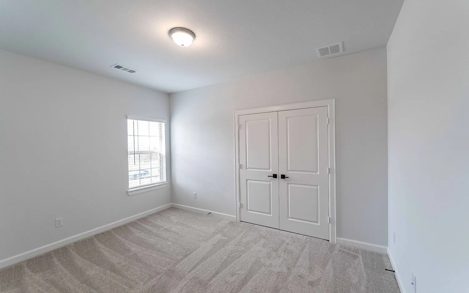 Light gray wall paint, textured gray carpeting, white trim, white paneled double doors with black hardware, and a single window with horizontal blinds