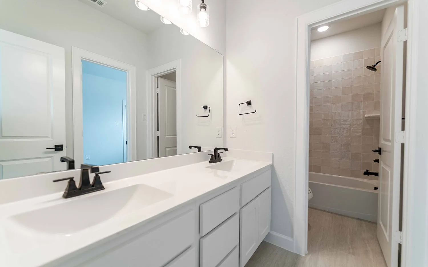 Dual vanity with white cabinetry, matte black fixtures, and a large mirror
