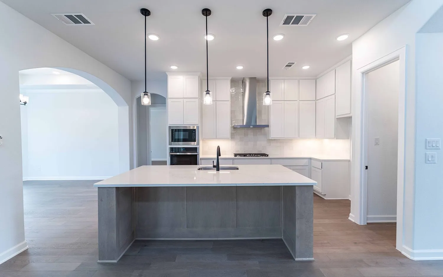 Kitchen island with a light-toned countertop, pendant lighting, built-in stainless steel appliances, white cabinetry, and wood-finish flooring
