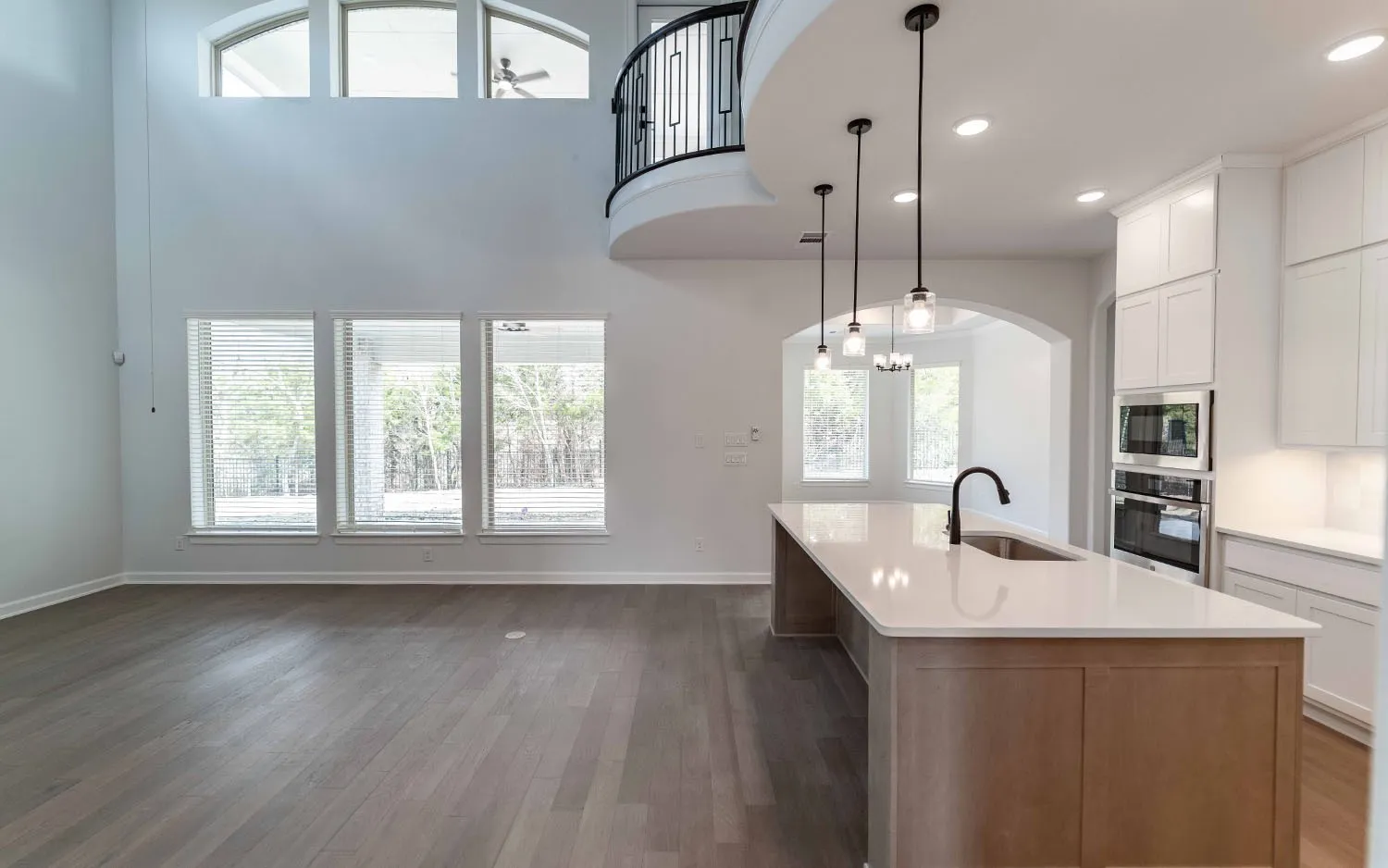 Two-story living area with wood-finish flooring, a kitchen island with a sink and pendant lighting, and built-in stainless steel appliances