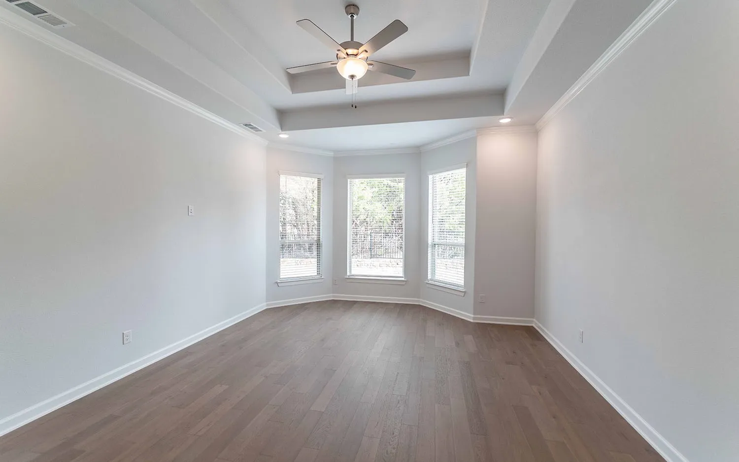 Tray ceiling with a ceiling fan, wood-finish flooring, and a bay window