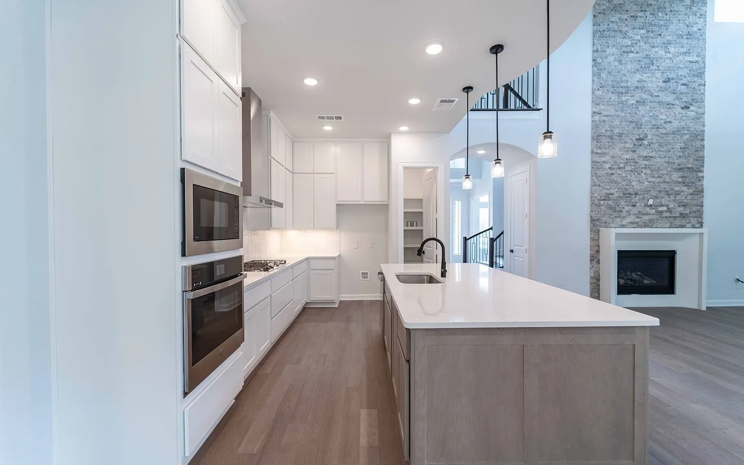 Kitchen featuring white cabinetry, stainless steel appliances, a center island with sink, and wood-finish flooring