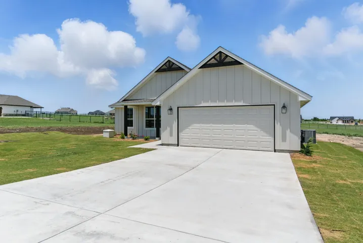 View of front facade with board and batten siding, cooling unit, concrete driveway, and a garage