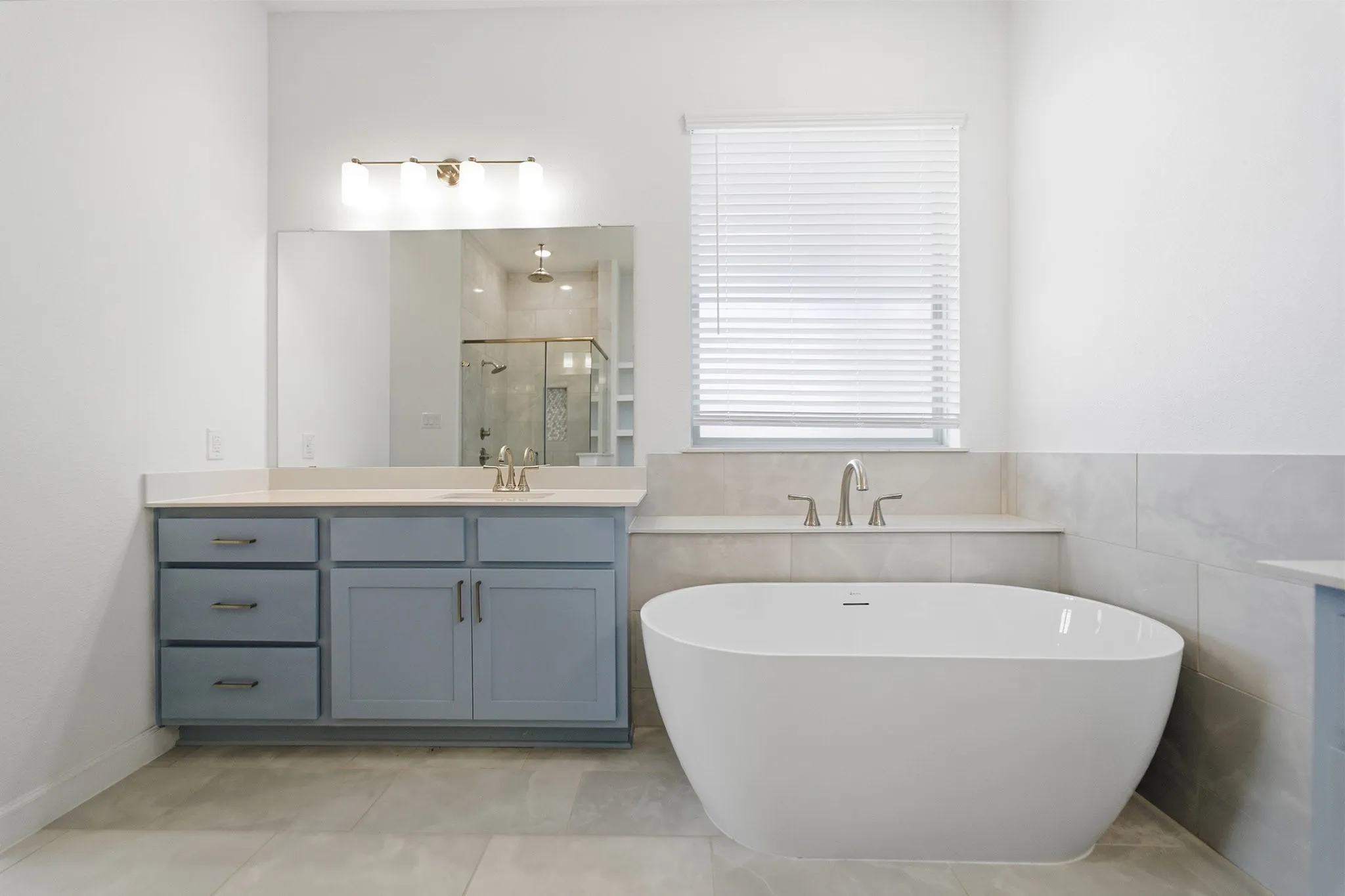 Freestanding soaking tub with a brushed nickel faucet, light blue vanity with a light-toned countertop, and a glass-enclosed shower with a rainfall showerhead