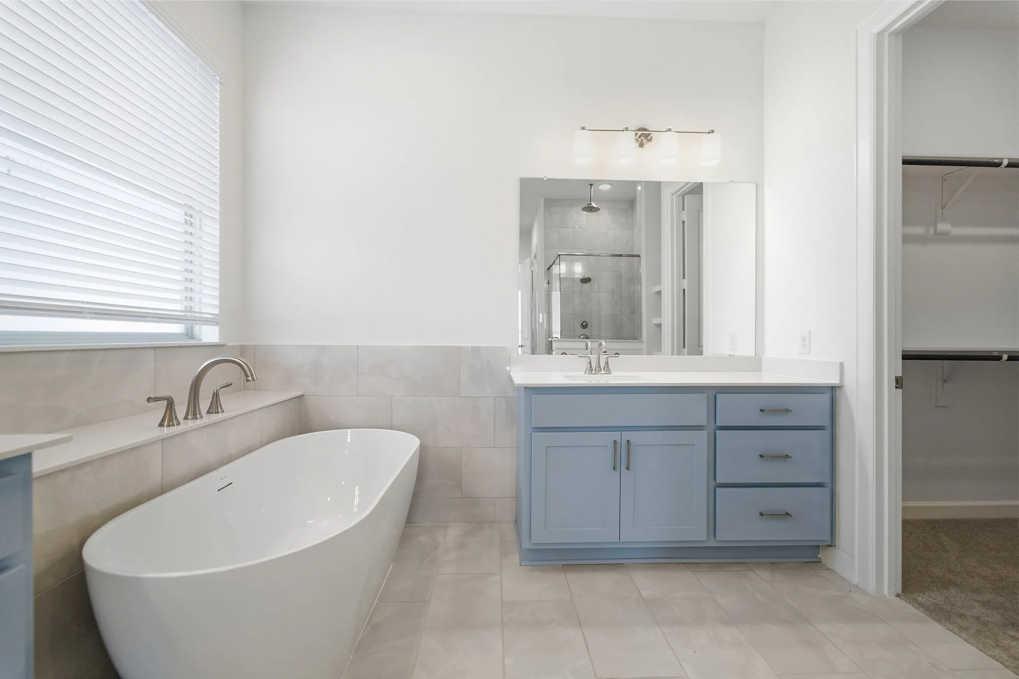 Modern bathroom featuring a freestanding soaking tub, single vanity with light blue cabinetry, white countertop, and brushed nickel fixtures
