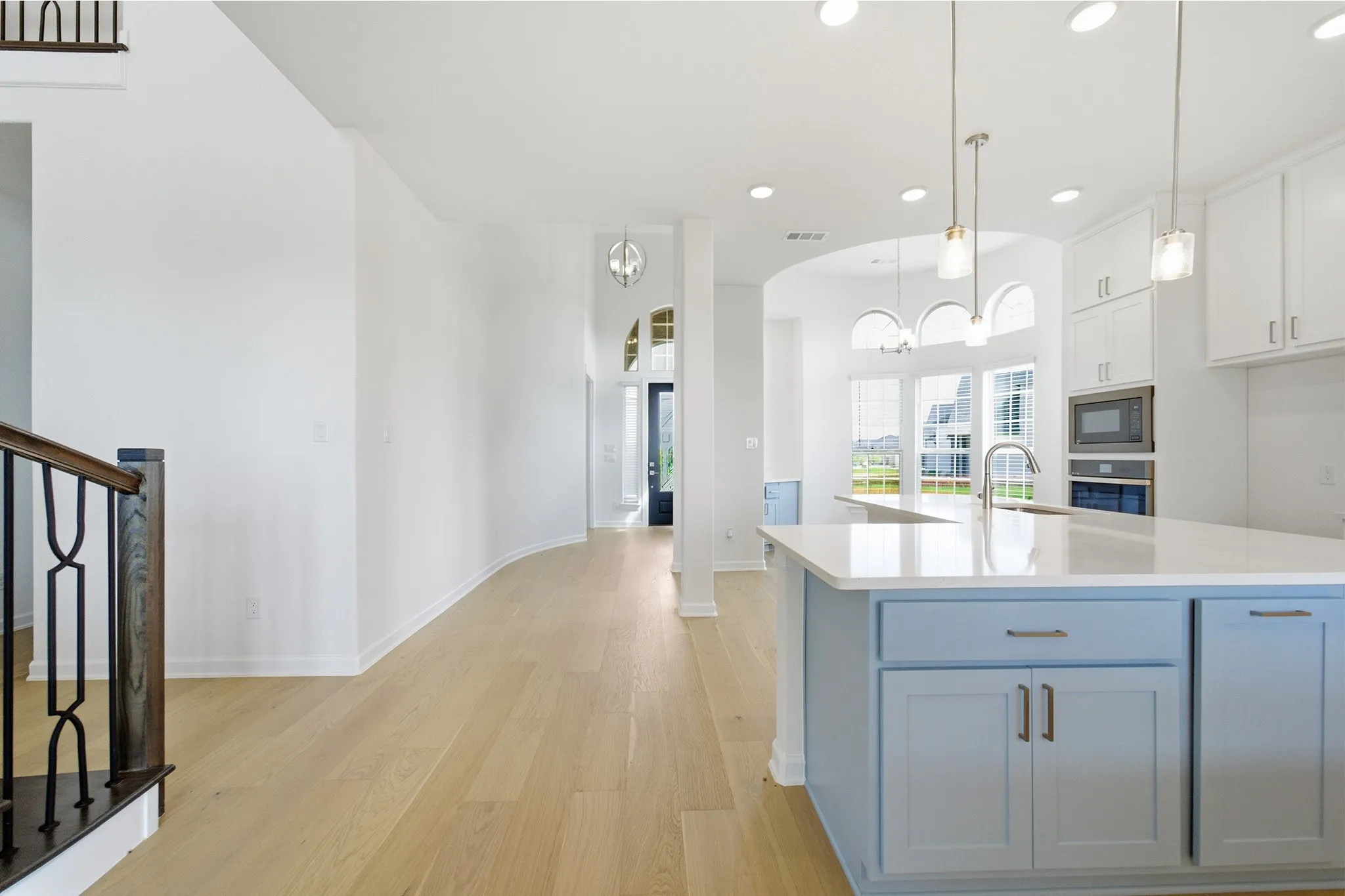 Open-concept kitchen featuring a light blue island with a white countertop, stainless steel appliances, and pendant lighting