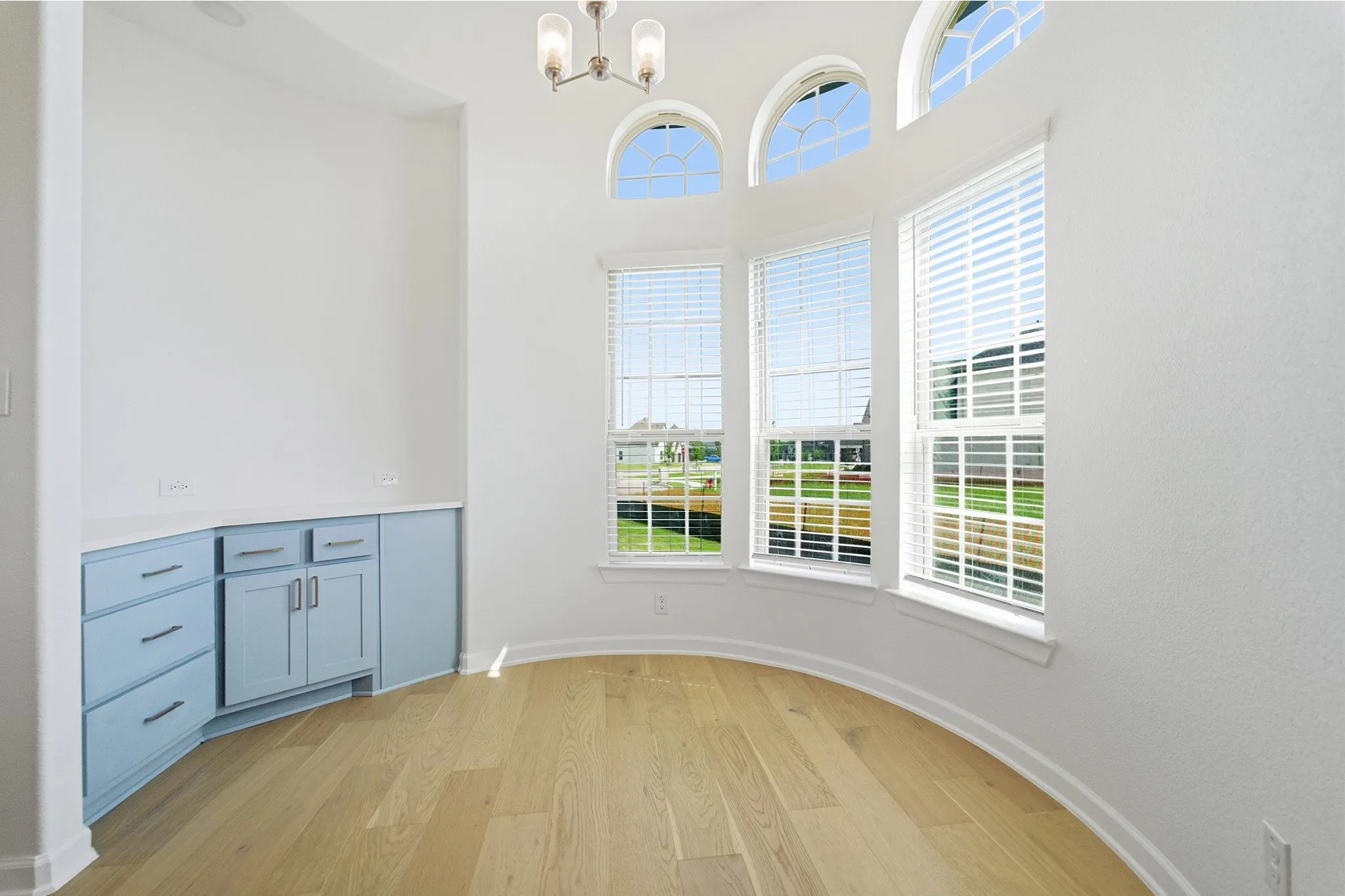 Curved bay window area featuring light wood-finish flooring and integrated cabinetry with a light blue finish and white countertop