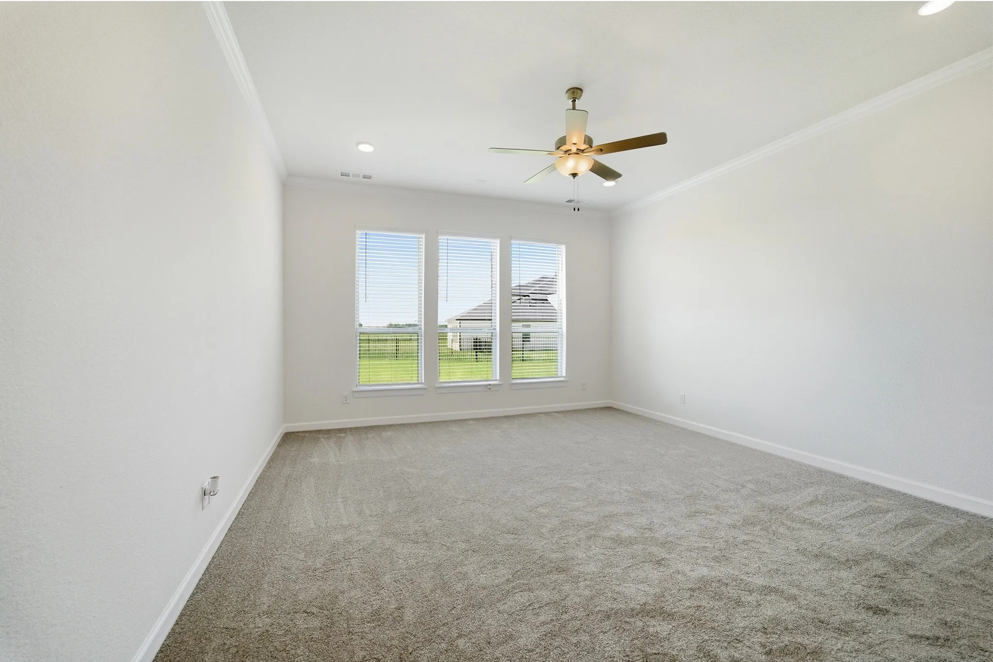 Spacious room featuring neutral carpeting, a triple window array with horizontal blinds, a ceiling fan with integrated lighting, recessed lighting, and crown molding