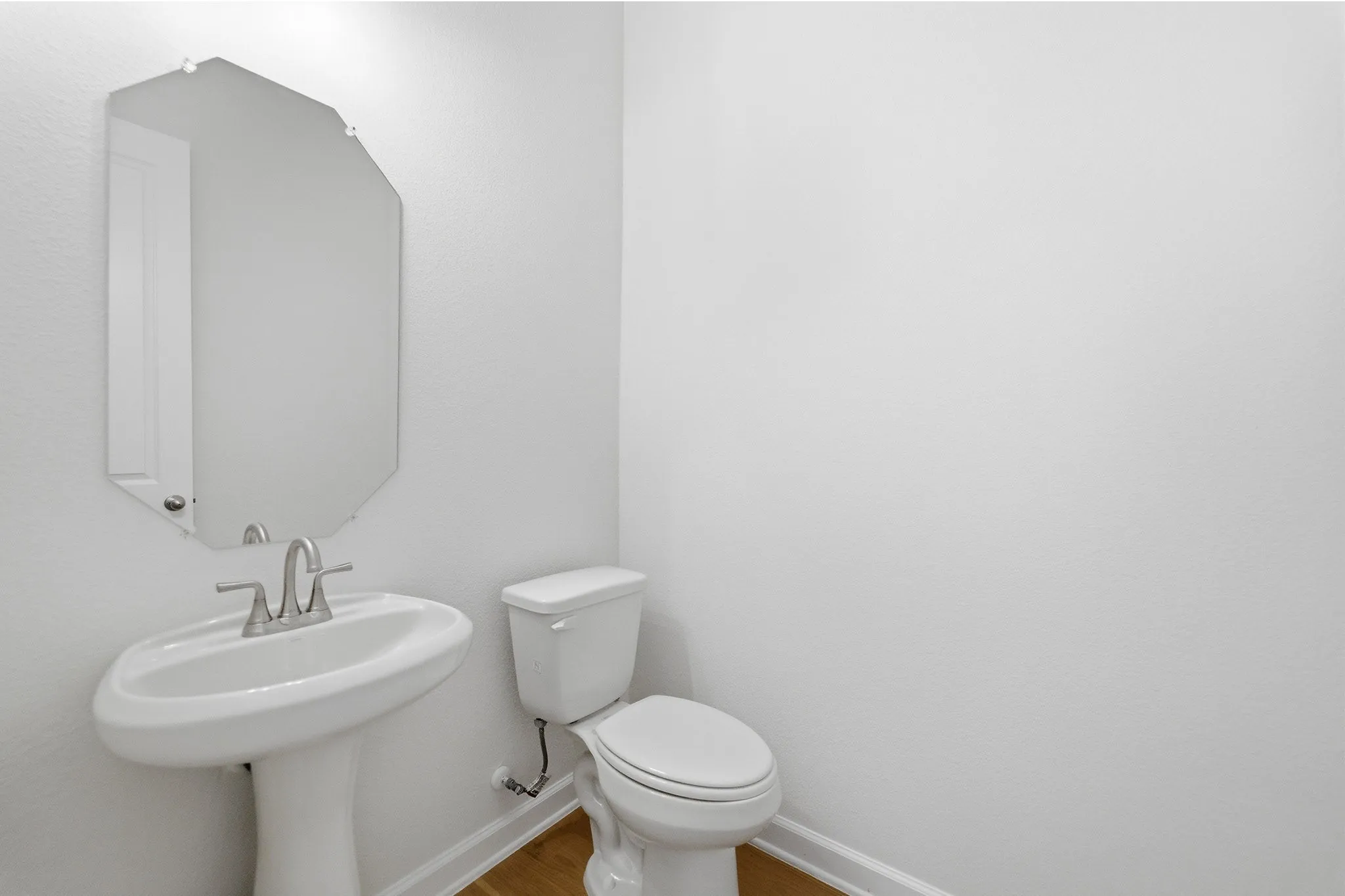 Pedestal sink with chrome faucet, octagonal wall mirror, and wood-finish flooring