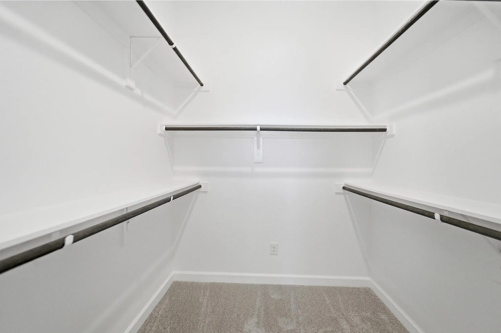 Walk-in closet featuring white walls, white shelving, dark hanging rods, light gray carpet, and white baseboards