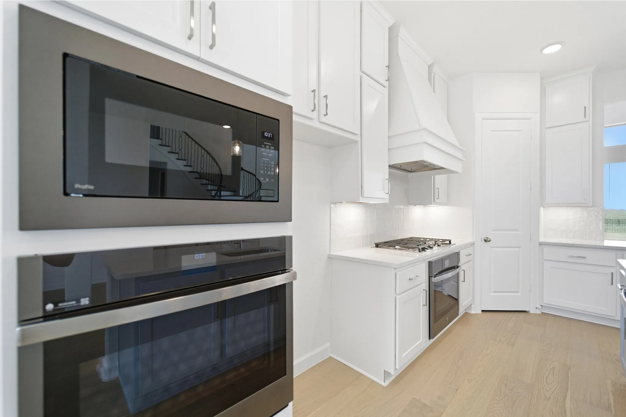 Kitchen featuring white shaker cabinetry, light wood-finish flooring, a built-in stainless steel microwave, a built-in stainless steel oven, and a gas cooktop with a custom range hood