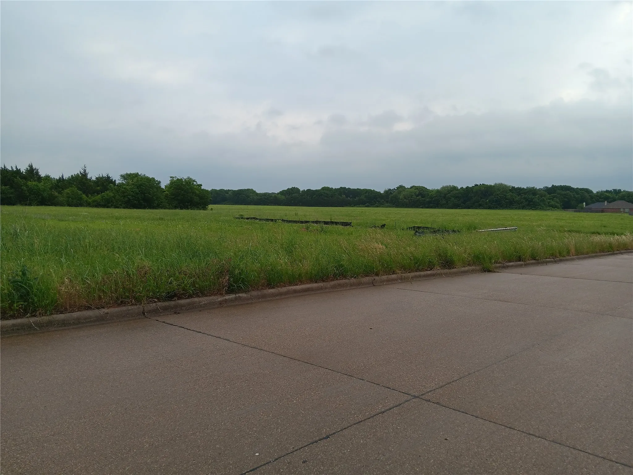 View of concrete road featuring curbs and a view of rural / pastoral area