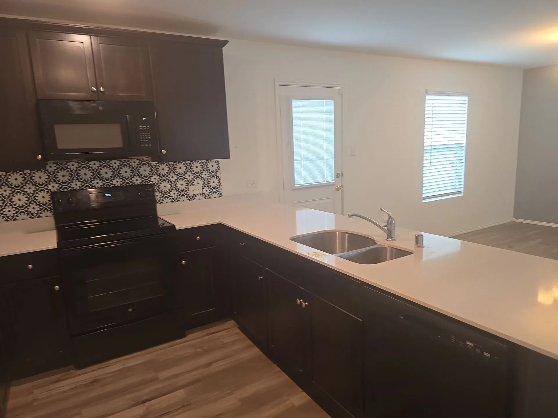 Kitchen featuring black appliances, light wood-type flooring, light countertops, backsplash, and a peninsula