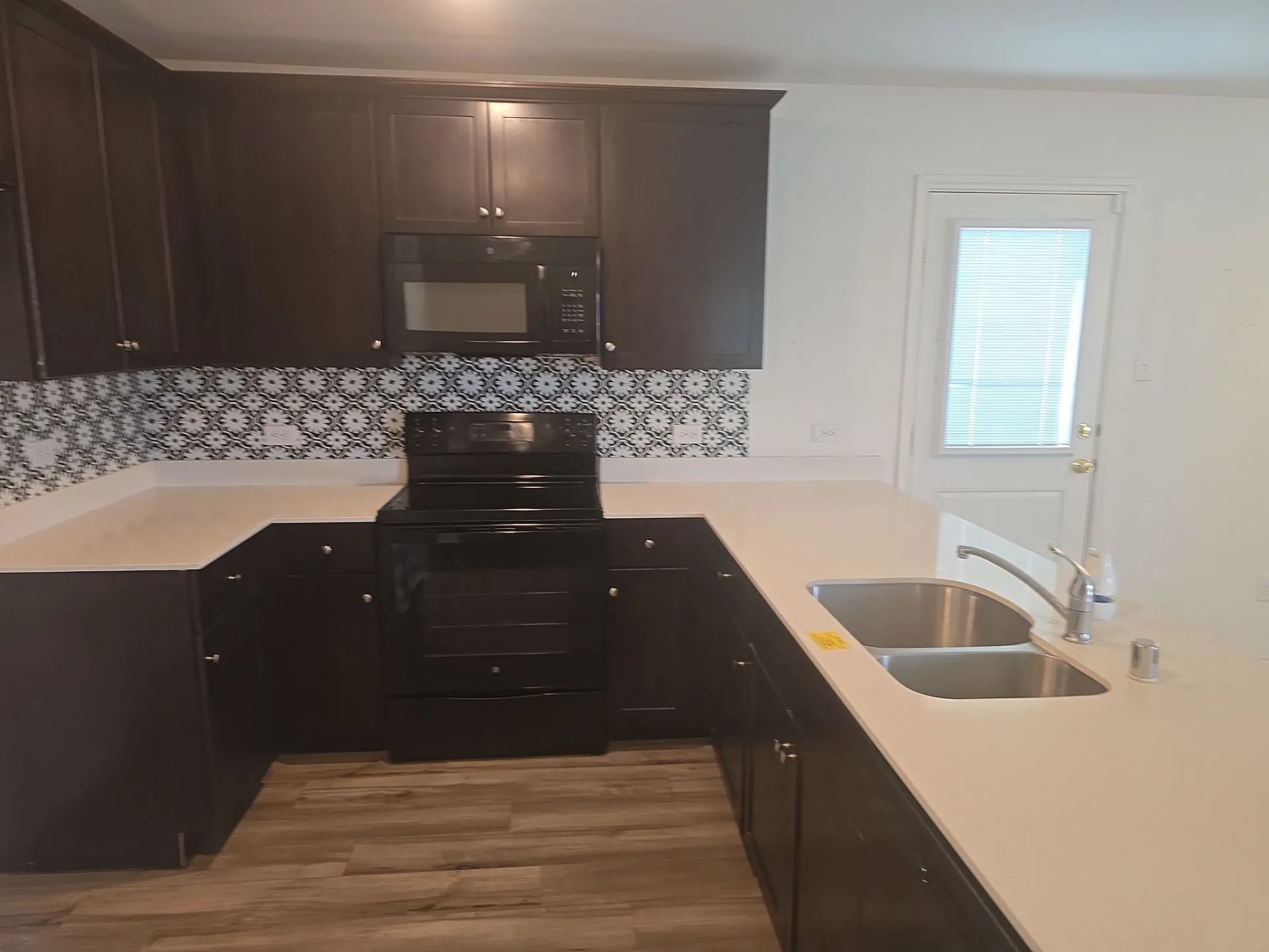 Kitchen with black appliances, wood finished floors, decorative backsplash, light countertops, and dark brown cabinetry