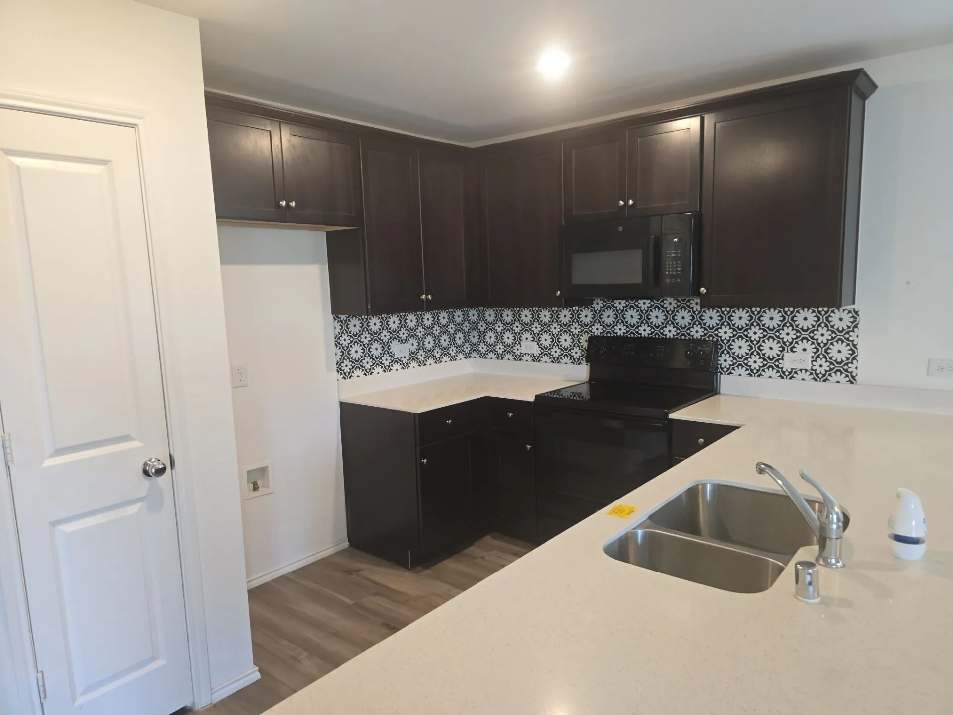 Kitchen with black appliances, wood finished floors, light countertops, and tasteful backsplash