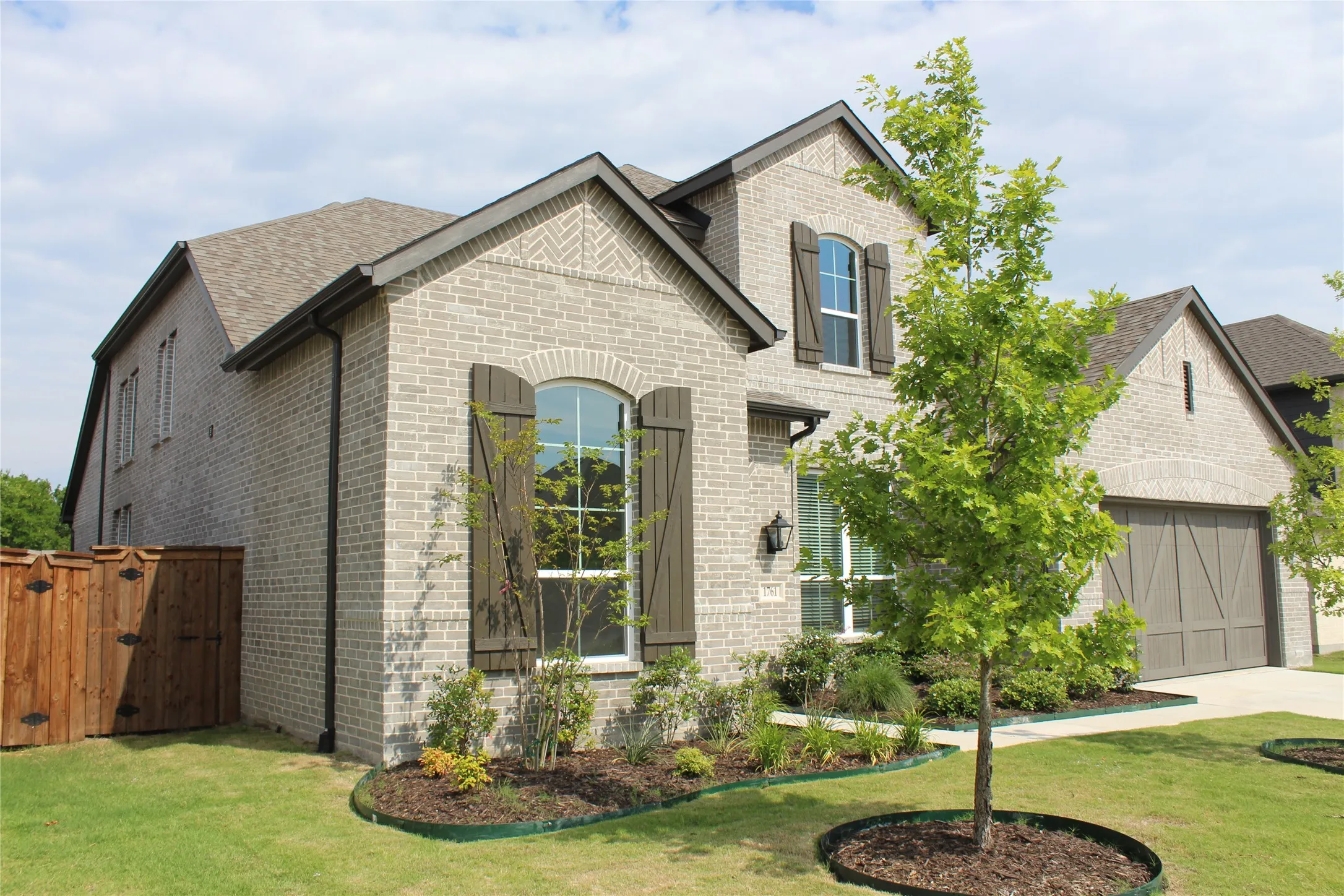 French country style house featuring brick siding, concrete driveway, roof with shingles, a gate, and a garage