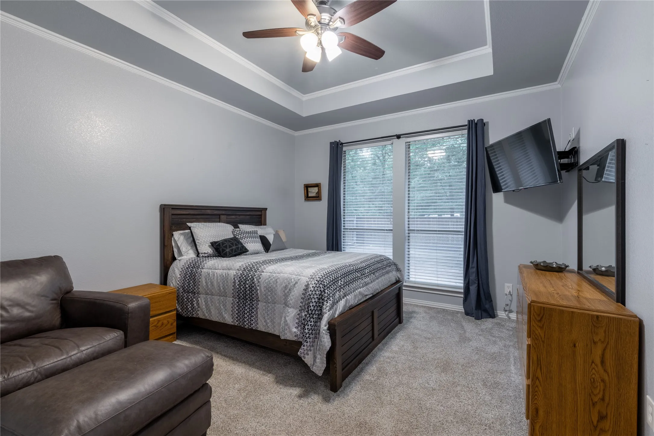 Carpeted bedroom featuring a raised ceiling, ceiling fan, and crown molding
