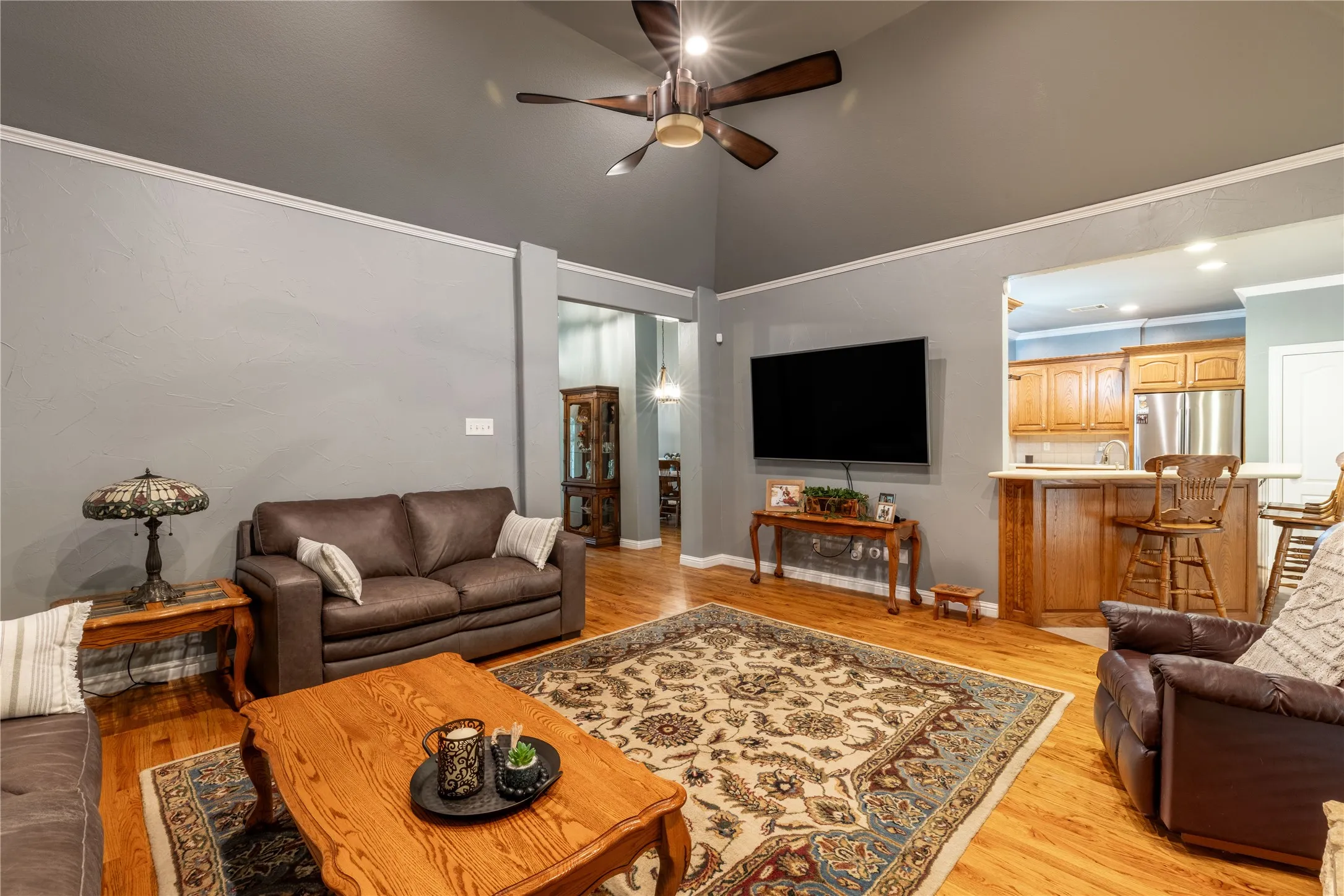 Living room with ceiling fan, high vaulted ceiling, and light wood-style flooring