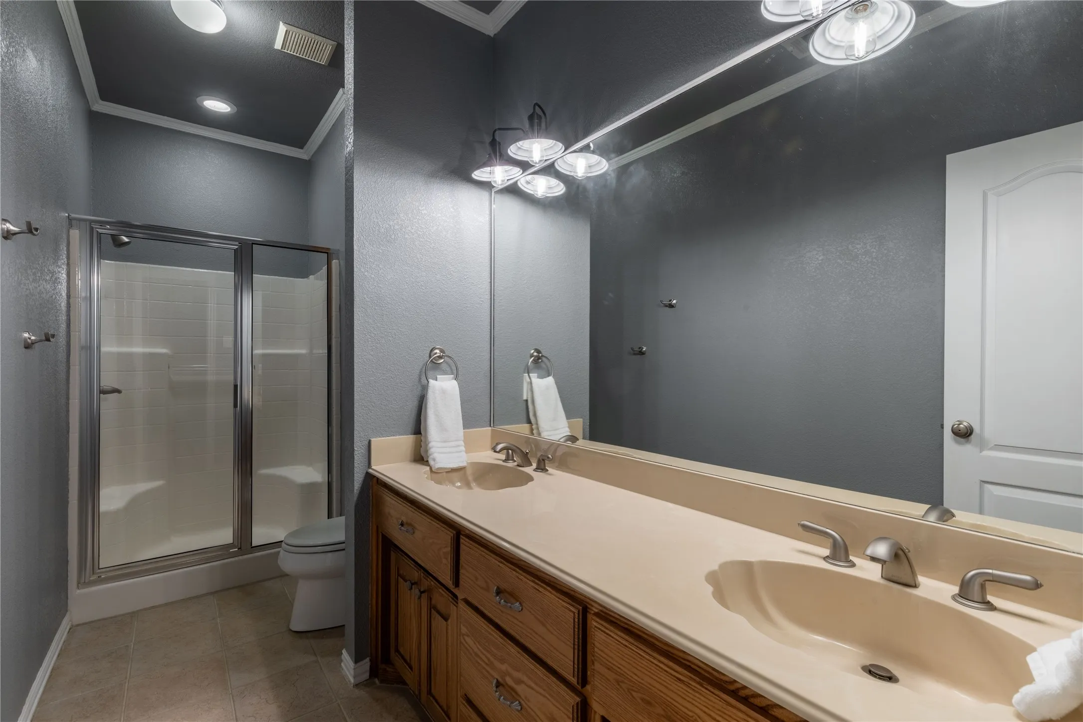 Full bathroom with crown molding, a shower stall, double vanity, tile patterned floors, and a textured wall