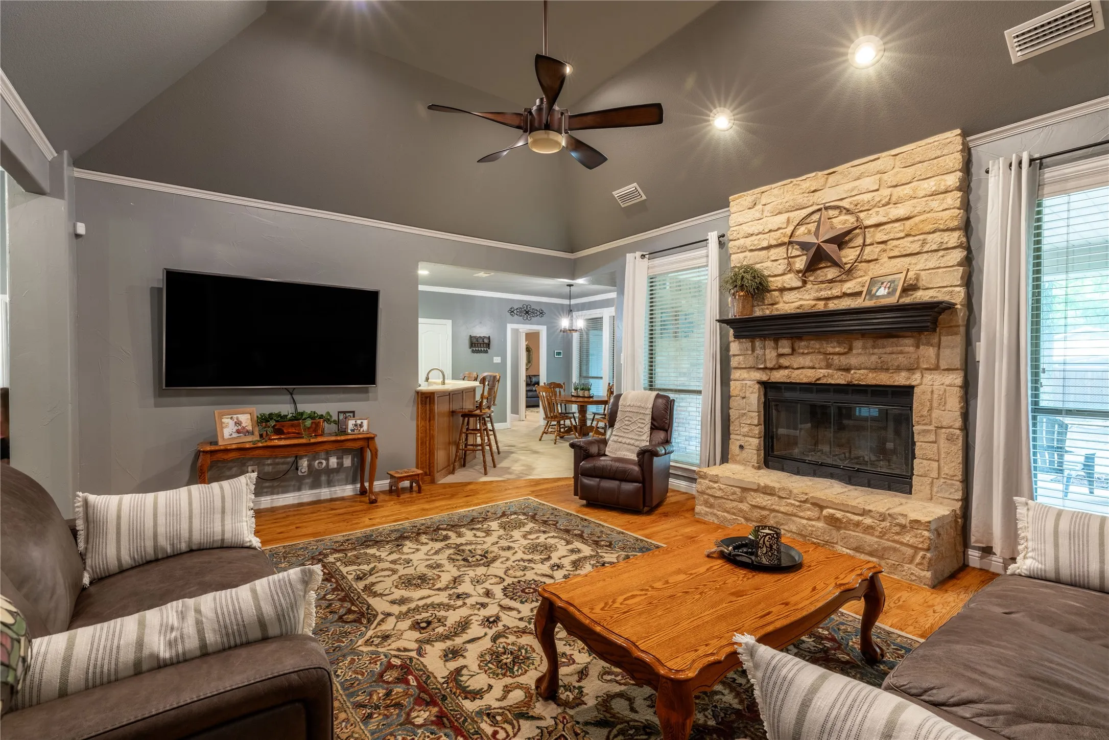 Living area with a ceiling fan, wood finished floors, high vaulted ceiling, and a fireplace