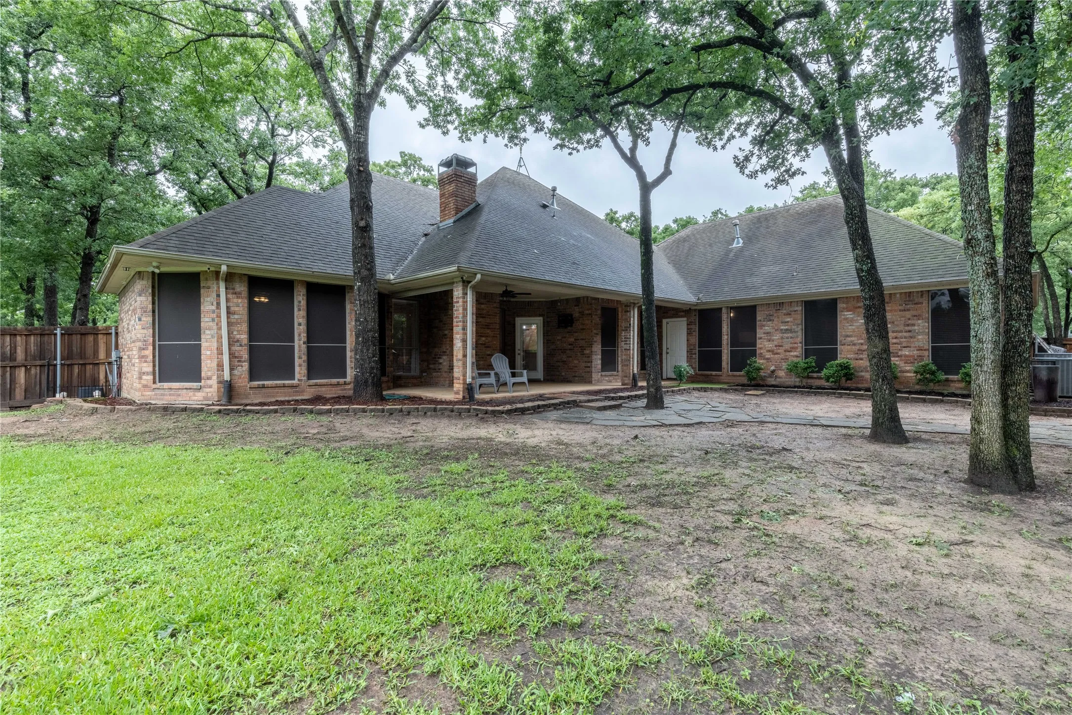 Rear view of house with a patio, a shingled roof, a chimney, and brick siding