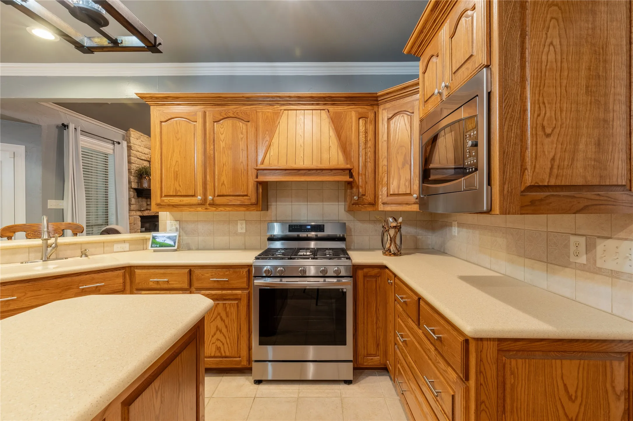 Kitchen featuring appliances with stainless steel finishes, custom exhaust hood, crown molding, light countertops, and brown cabinets