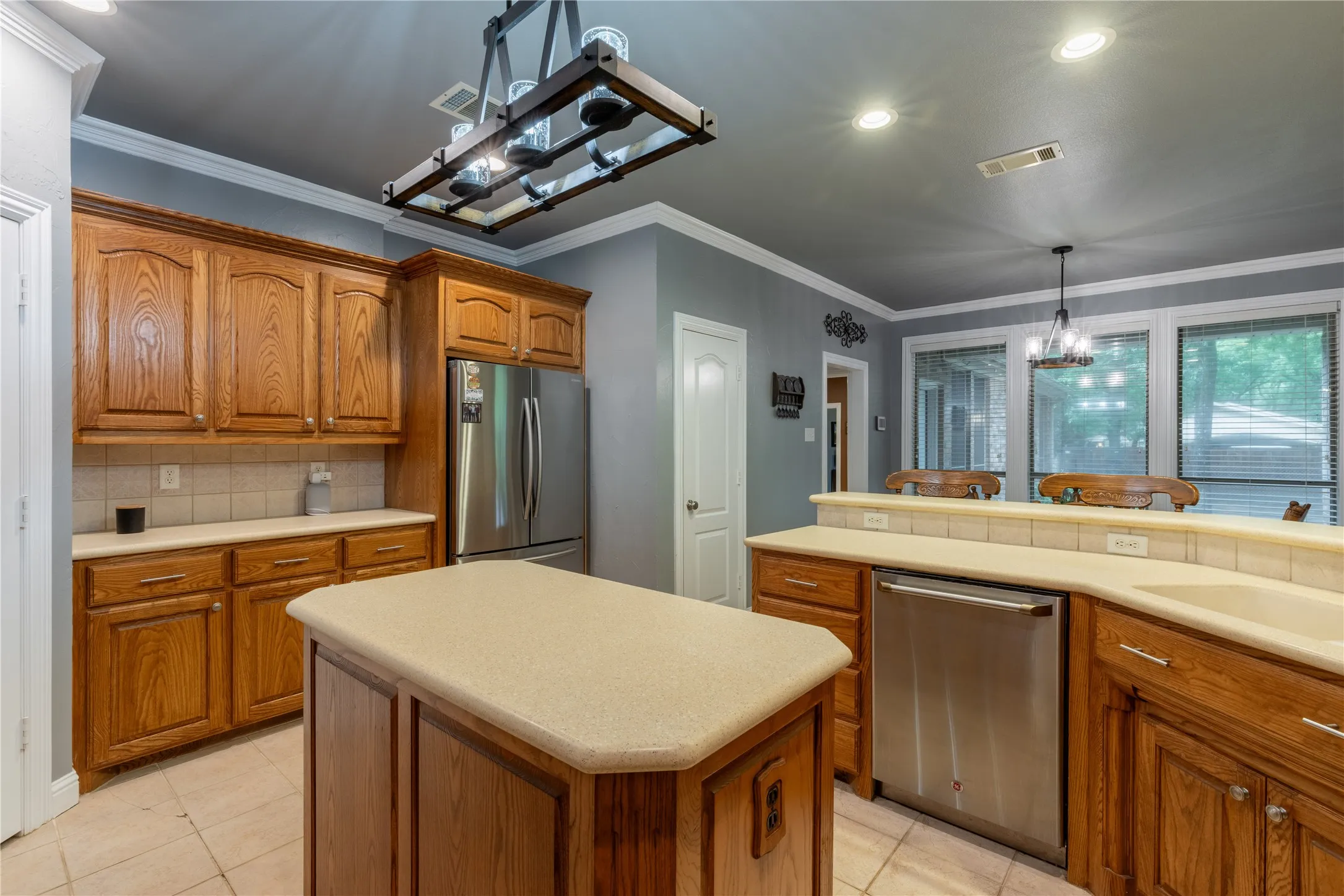 Kitchen featuring appliances with stainless steel finishes, brown cabinetry, a chandelier, light countertops, and ornamental molding