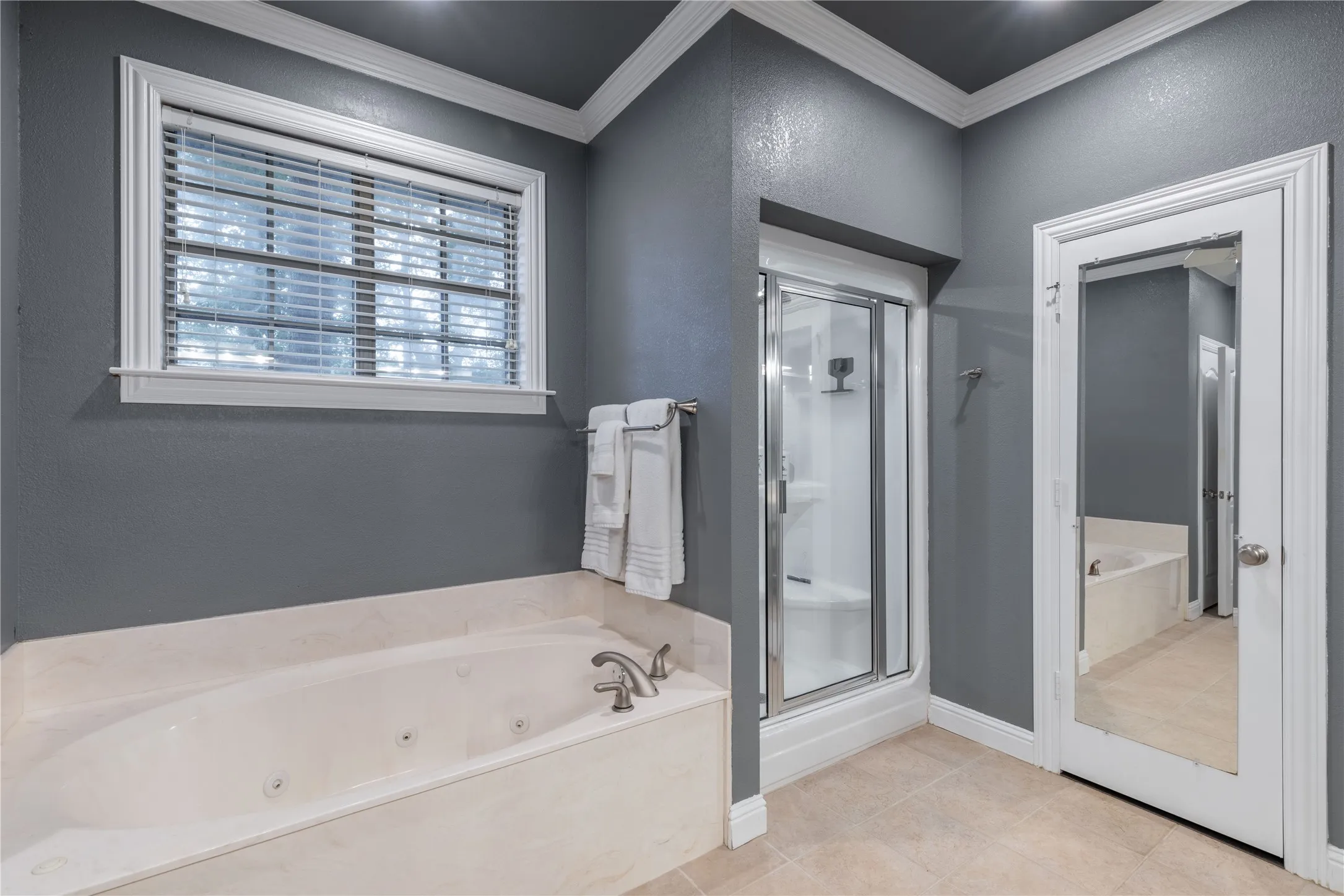 Bathroom featuring a stall shower, a whirlpool tub, crown molding, and tile patterned flooring