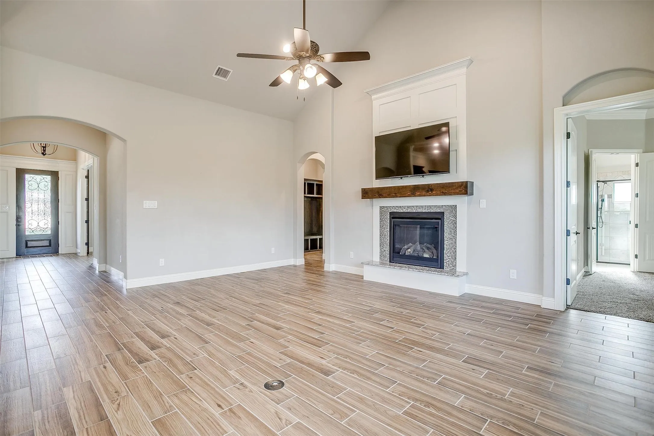 Unfurnished living room featuring arched walkways, ceiling fan, high vaulted ceiling, light wood-type flooring, and a tile fireplace