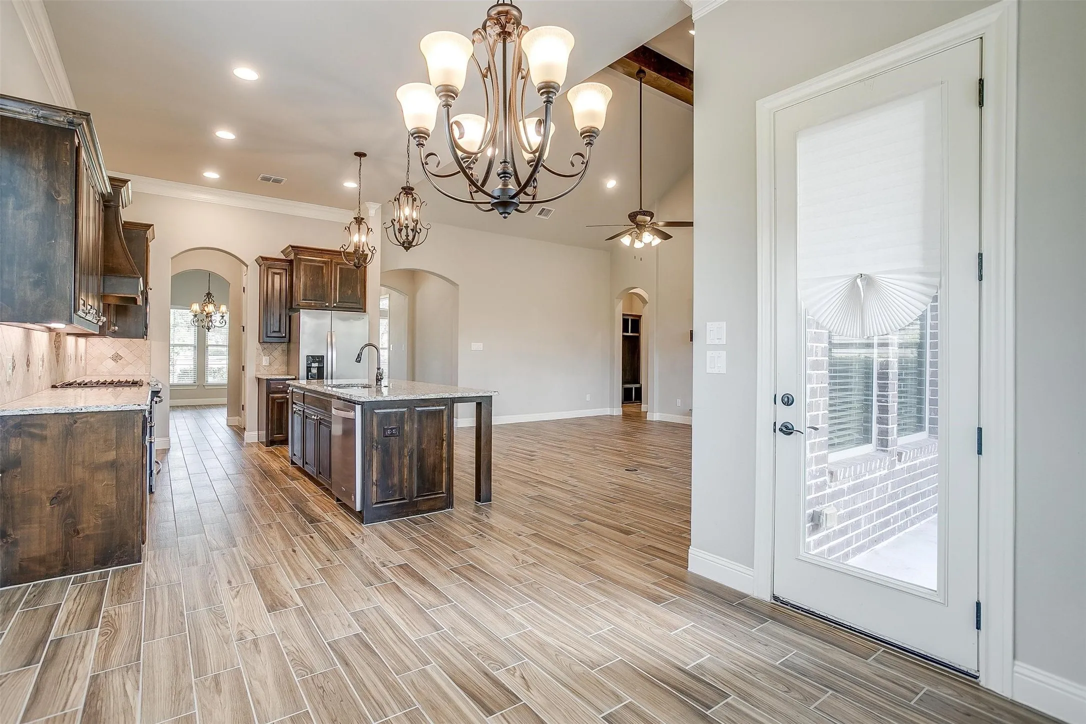 Kitchen with arched walkways, a chandelier, dark brown cabinetry, ceiling fan, and beamed ceiling