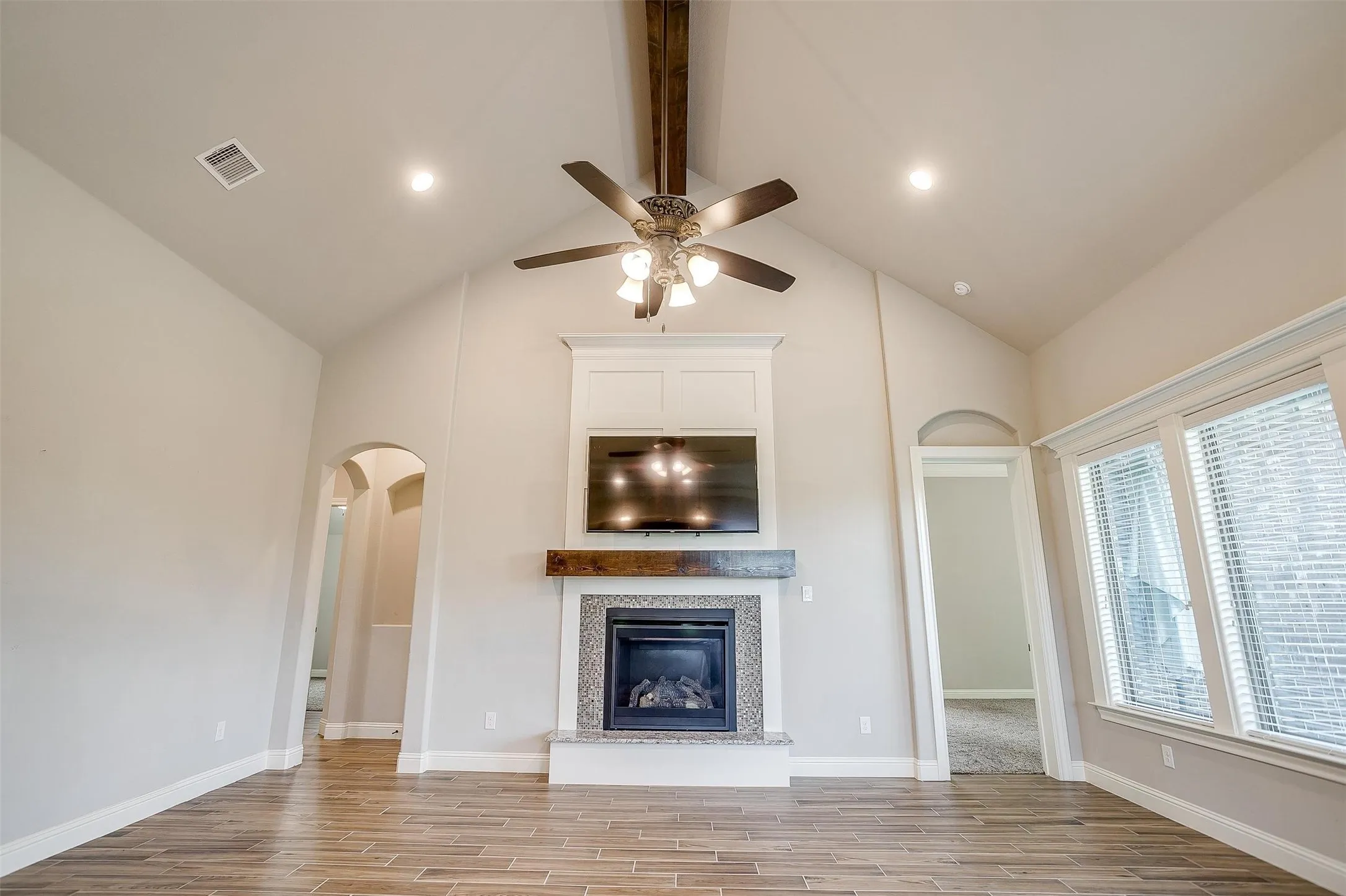 Unfurnished living room featuring high vaulted ceiling, ceiling fan, wood finished floors, a tile fireplace, and arched walkways