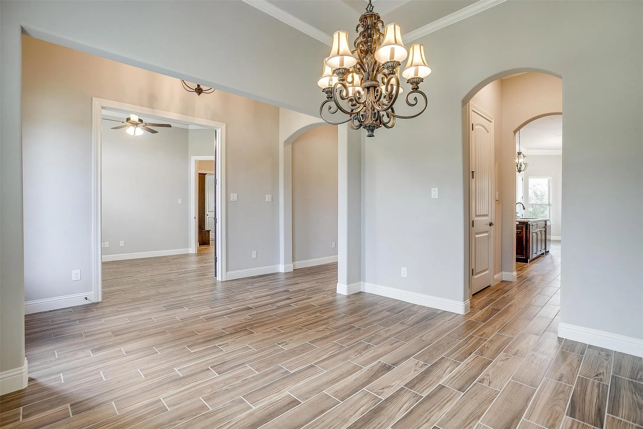 Empty room with ornamental molding, arched walkways, light wood finished floors, ceiling fan, and a chandelier