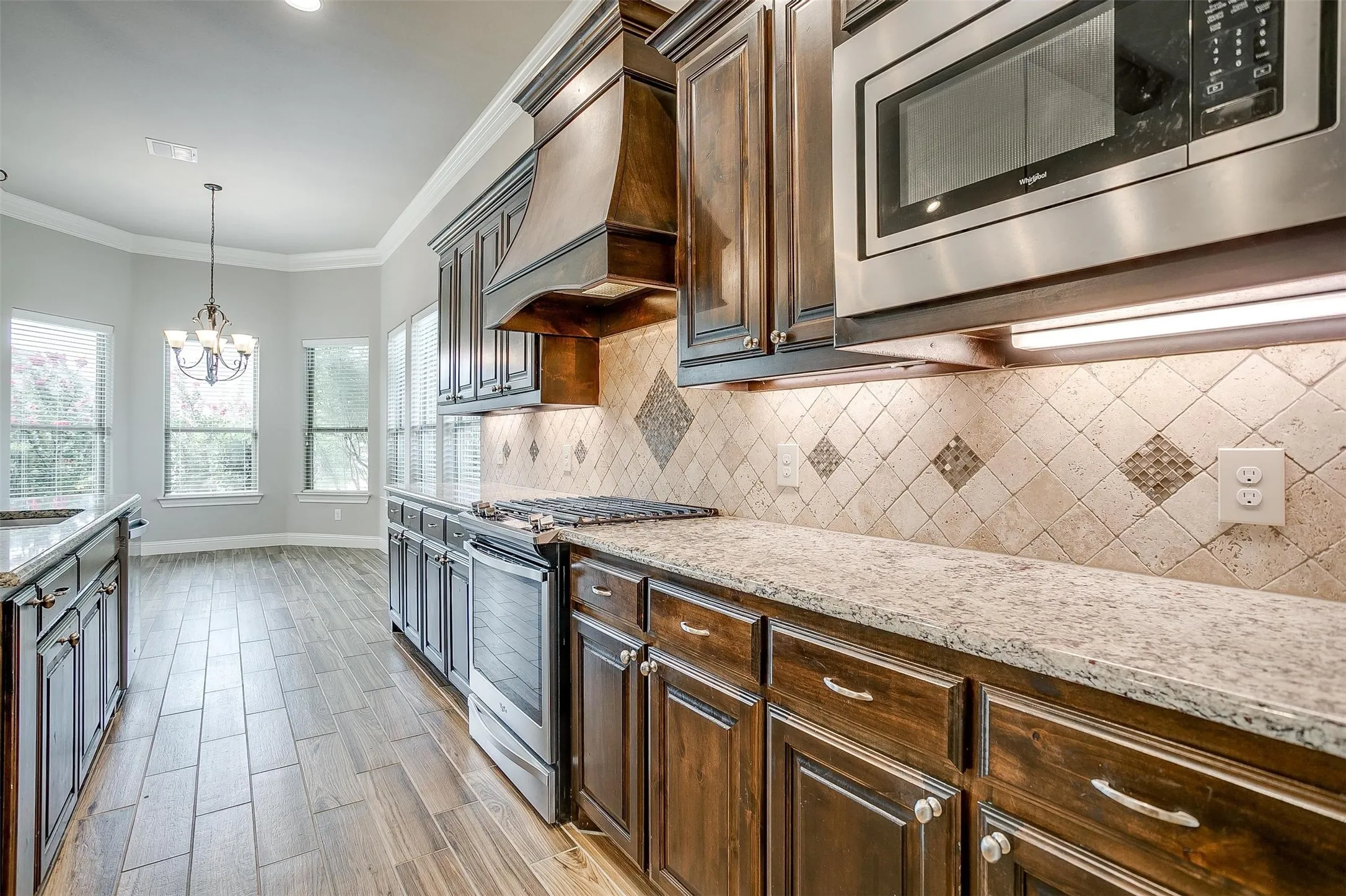 Kitchen with stainless steel appliances, premium range hood, dark brown cabinets, tasteful backsplash, and crown molding