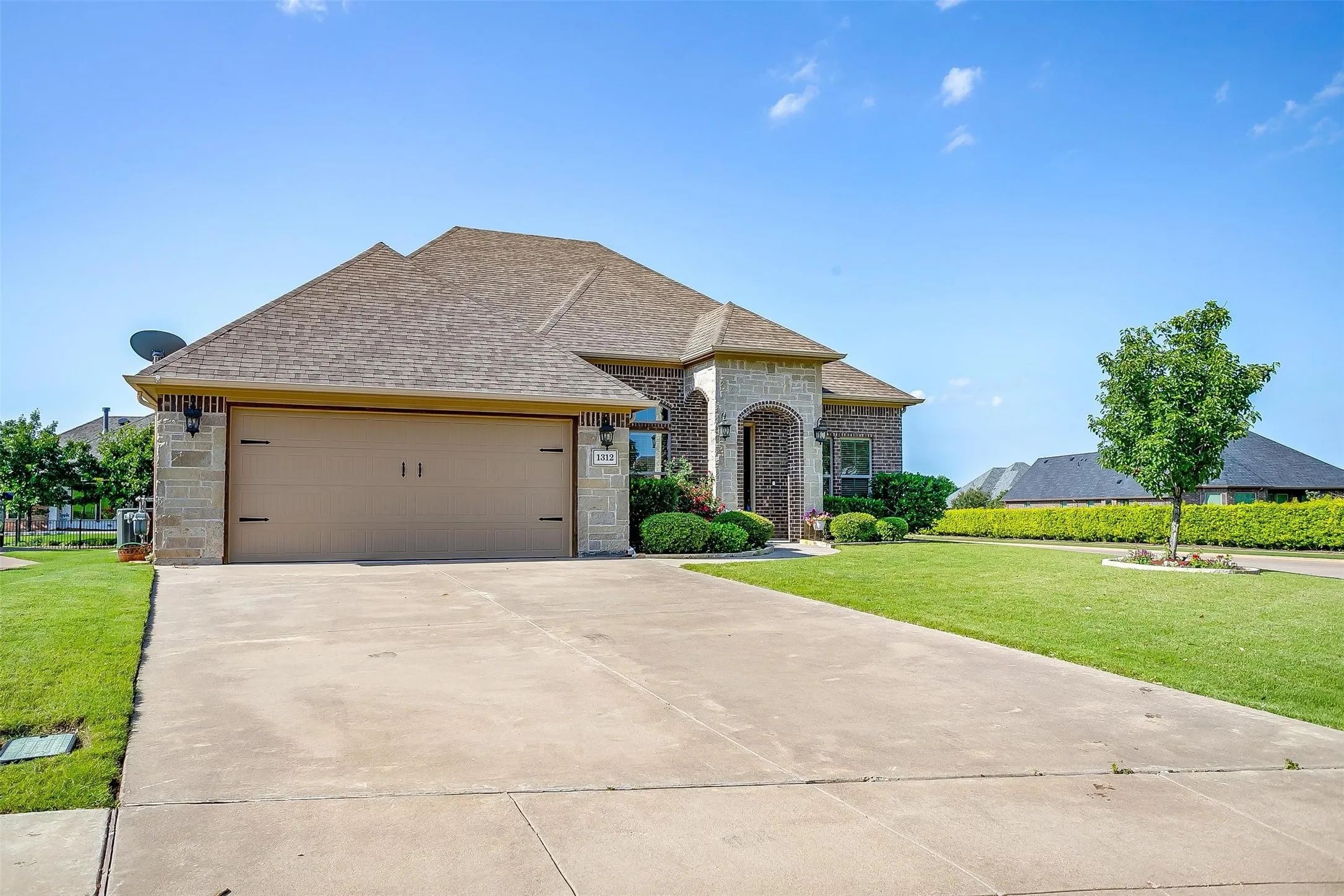 French country inspired facade with a front lawn, roof with shingles, an attached garage, driveway, and brick siding
