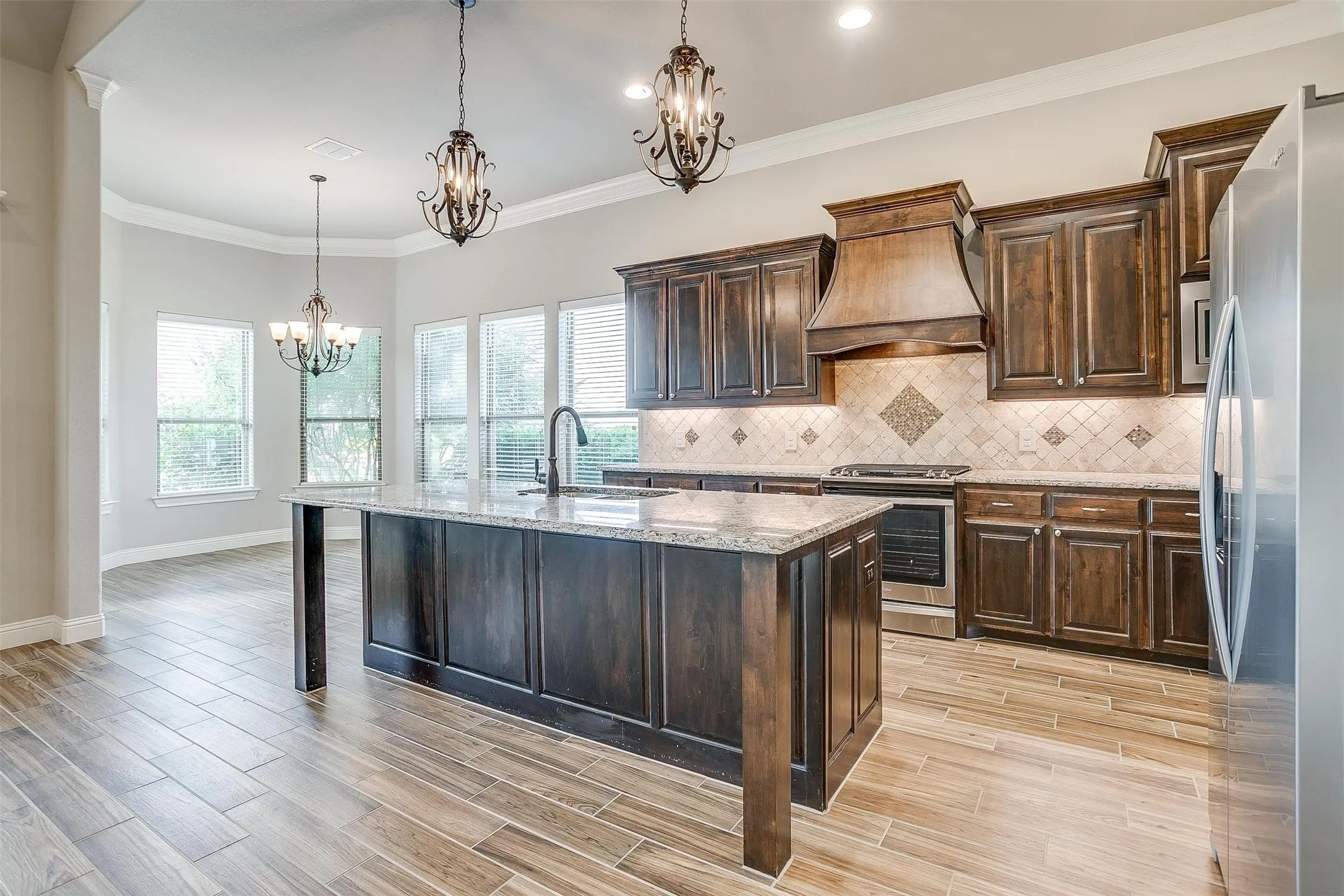 Kitchen with stainless steel appliances, a chandelier, custom exhaust hood, light stone counters, and healthy amount of natural light