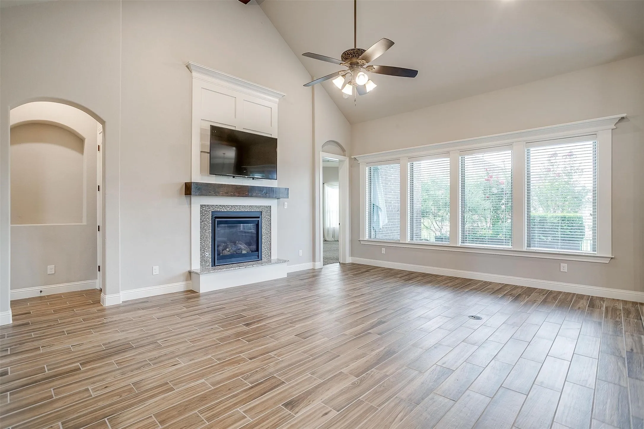Unfurnished living room with ceiling fan, light wood-style flooring, high vaulted ceiling, and a glass covered fireplace