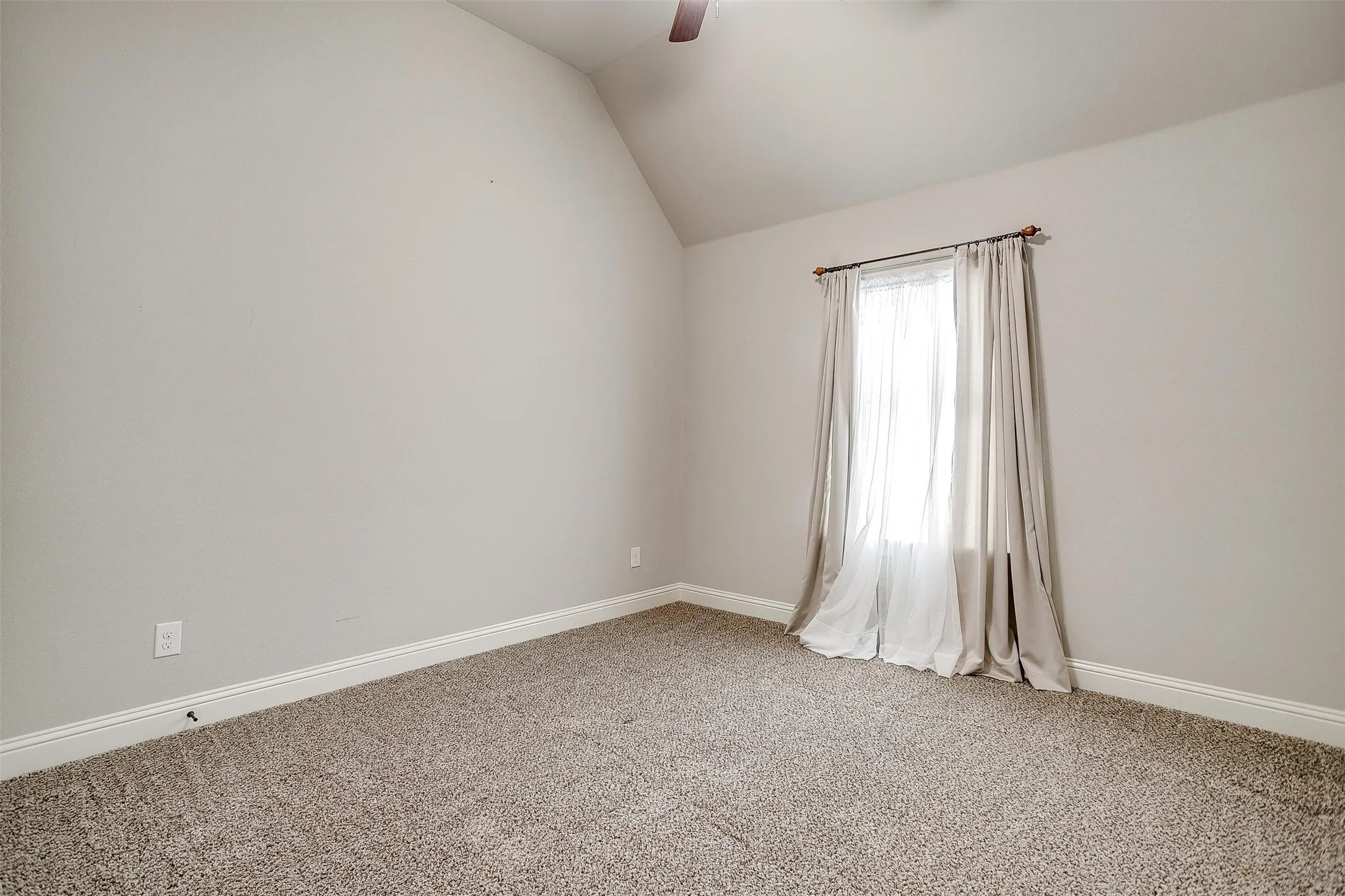 Carpeted empty room with vaulted ceiling and a ceiling fan