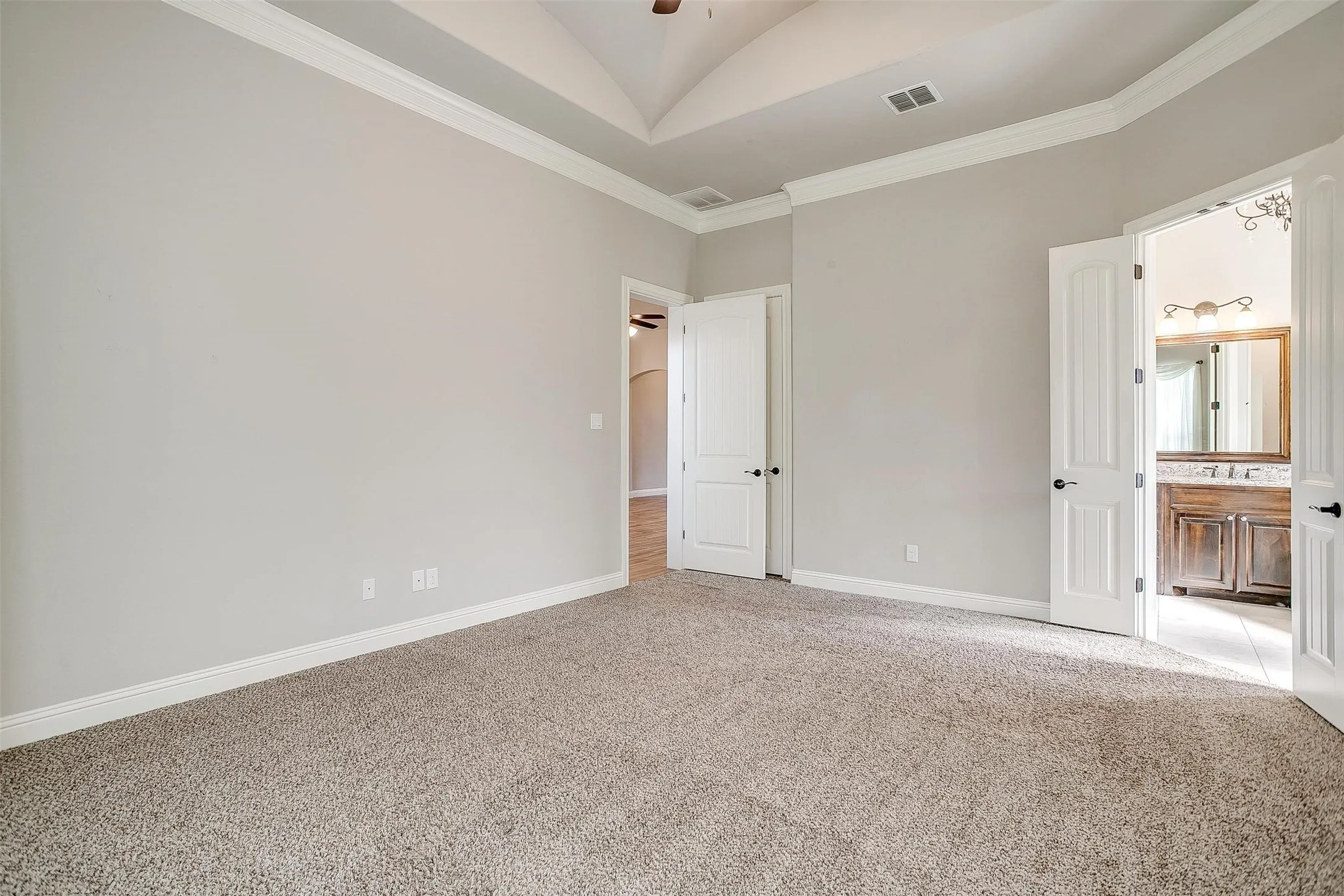 Unfurnished bedroom with light carpet, vaulted ceiling, ornamental molding, and ensuite bathroom