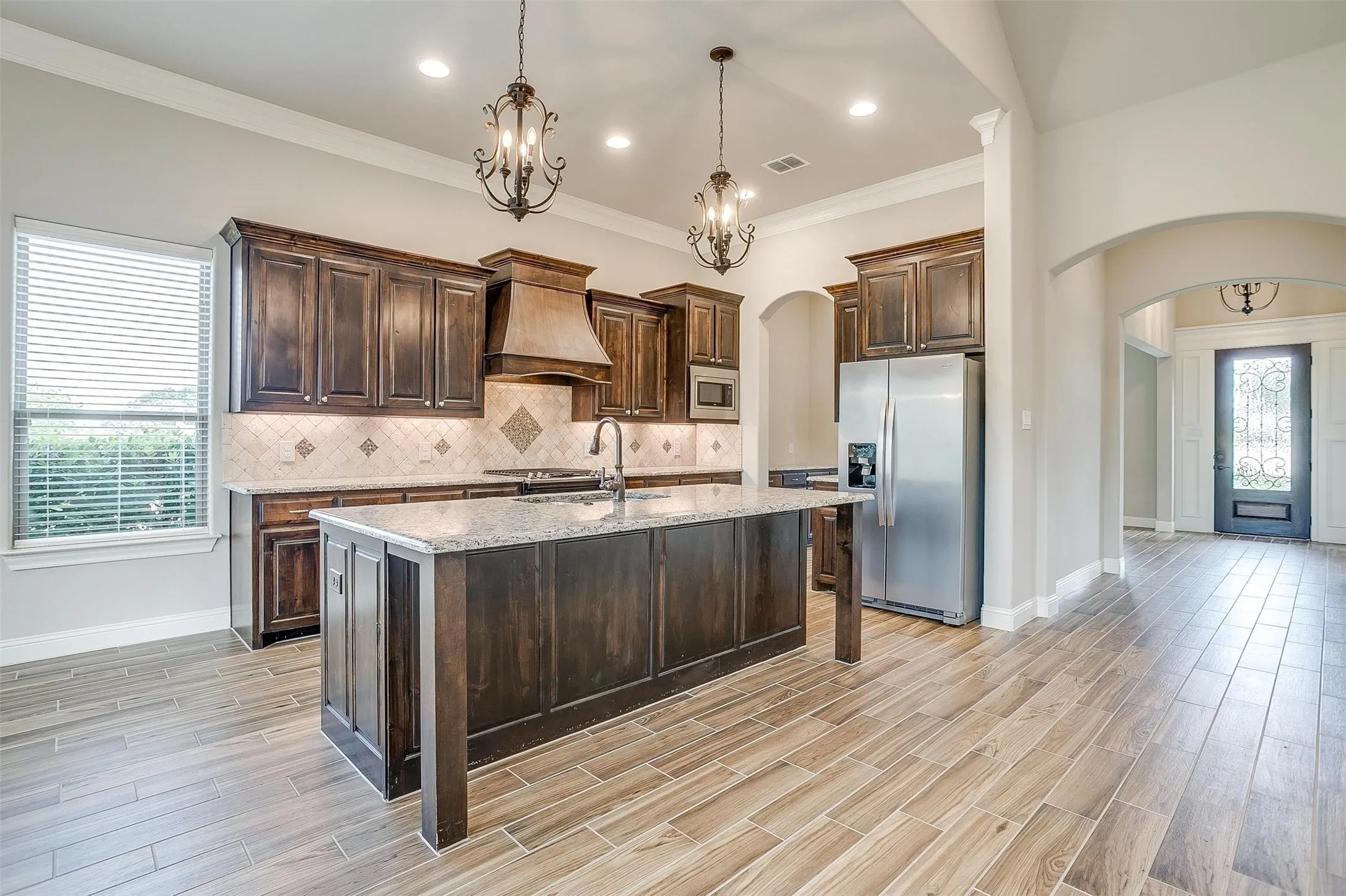 Kitchen with appliances with stainless steel finishes, arched walkways, custom exhaust hood, tasteful backsplash, and dark brown cabinets
