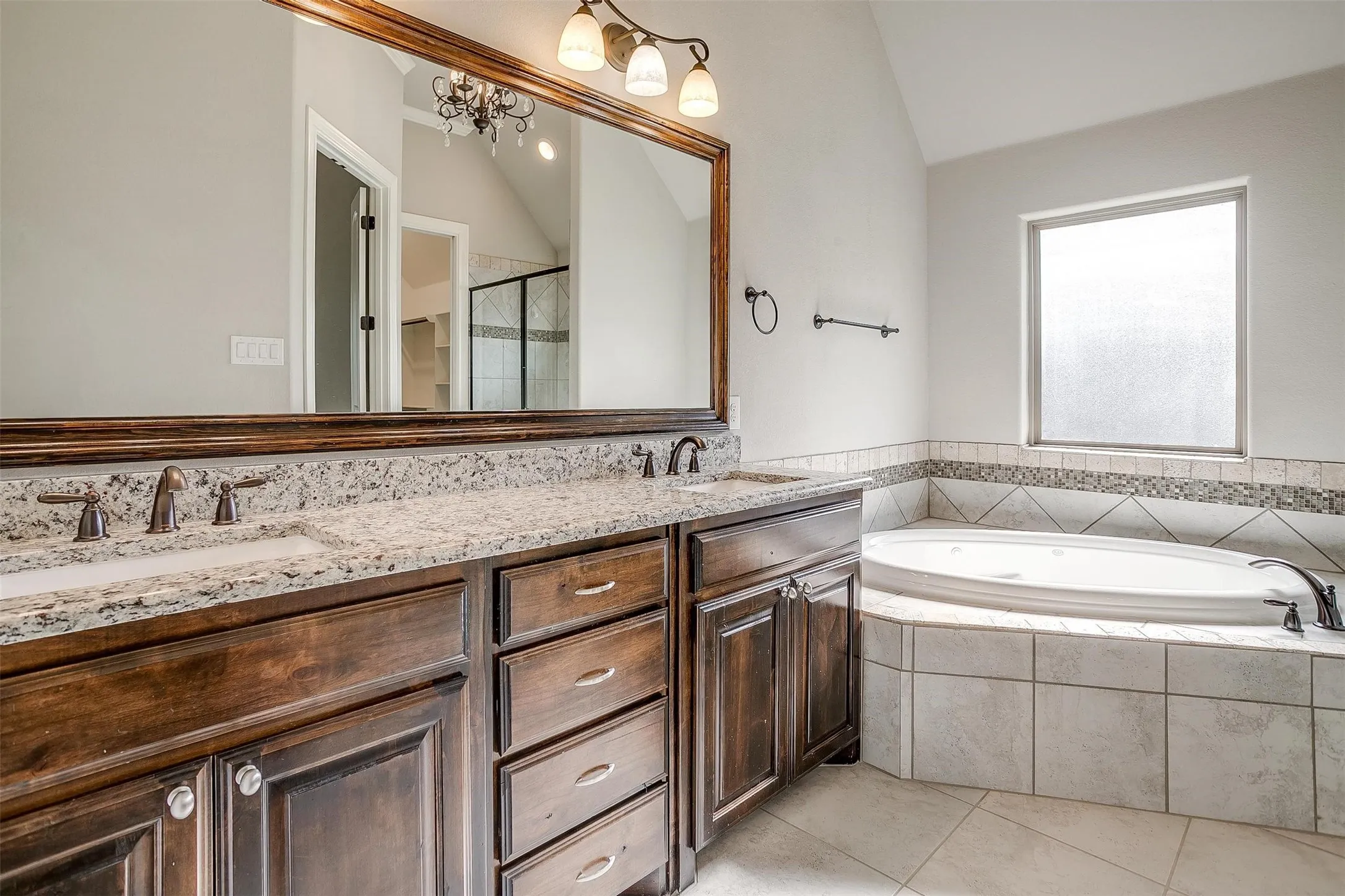 Bathroom with vaulted ceiling, a bath, double vanity, tile patterned flooring, and a tile shower