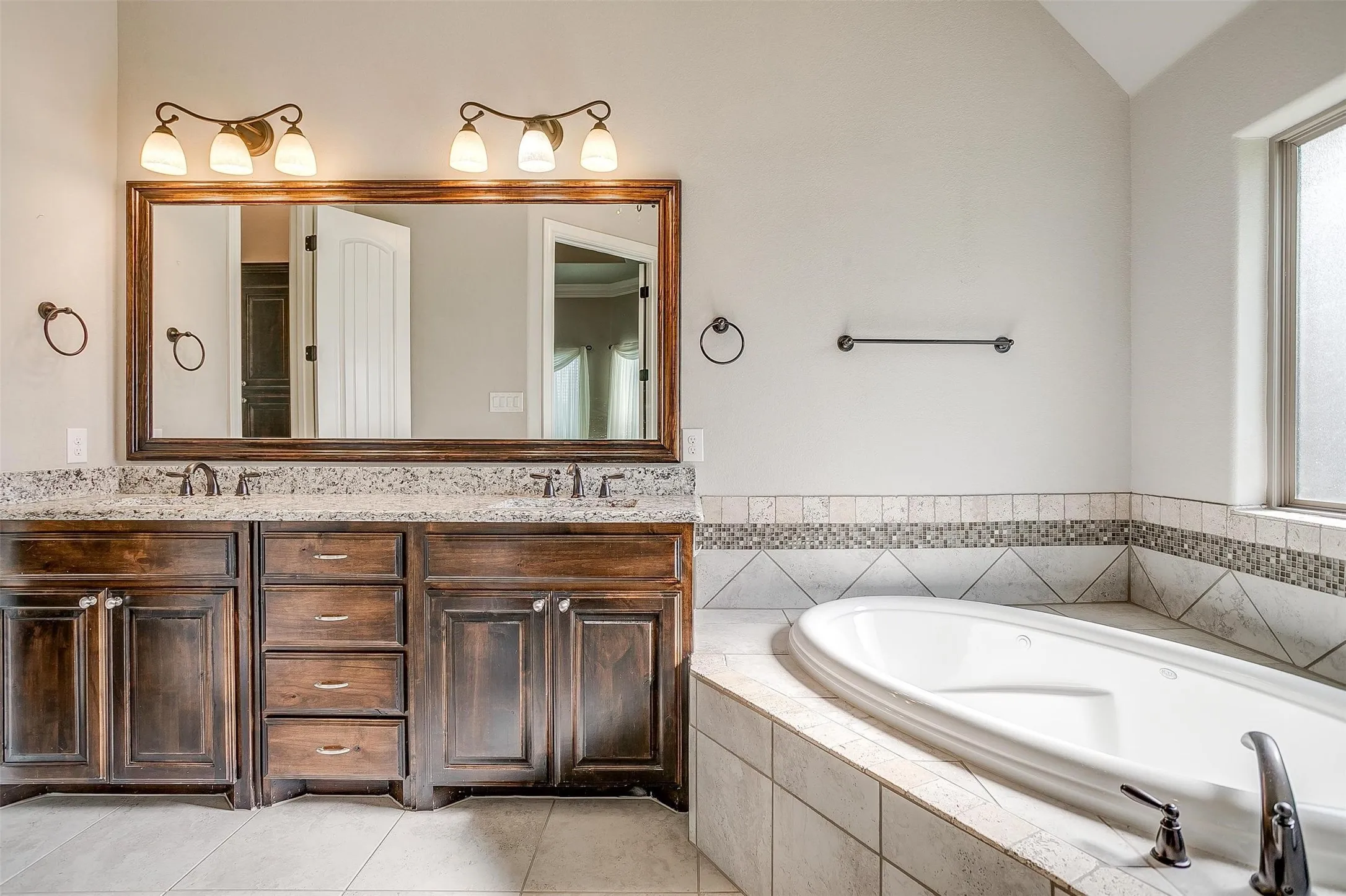 Bathroom with double vanity, a bath, tile patterned floors, and lofted ceiling